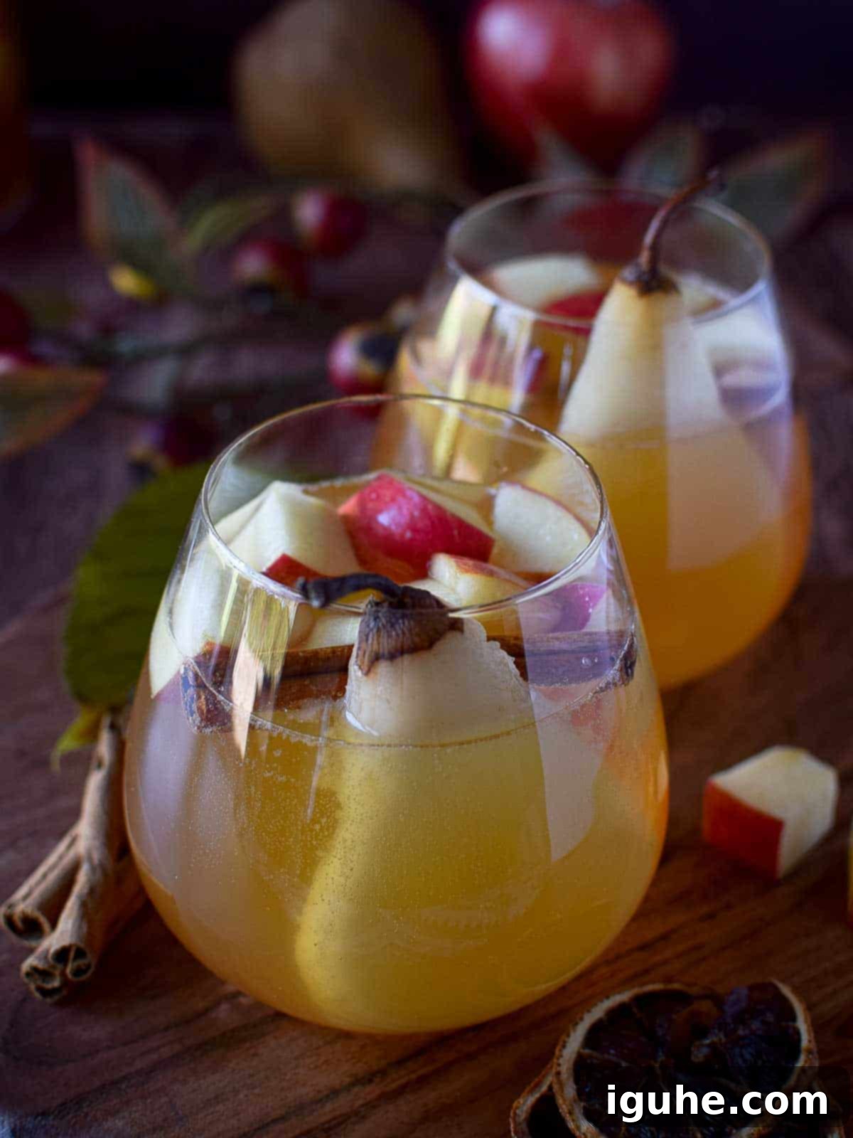 Autumn Orchard White Sangria 4 Close-up of two glasses of apple and pear sangria, garnished with pear slices and cinnamon sticks.