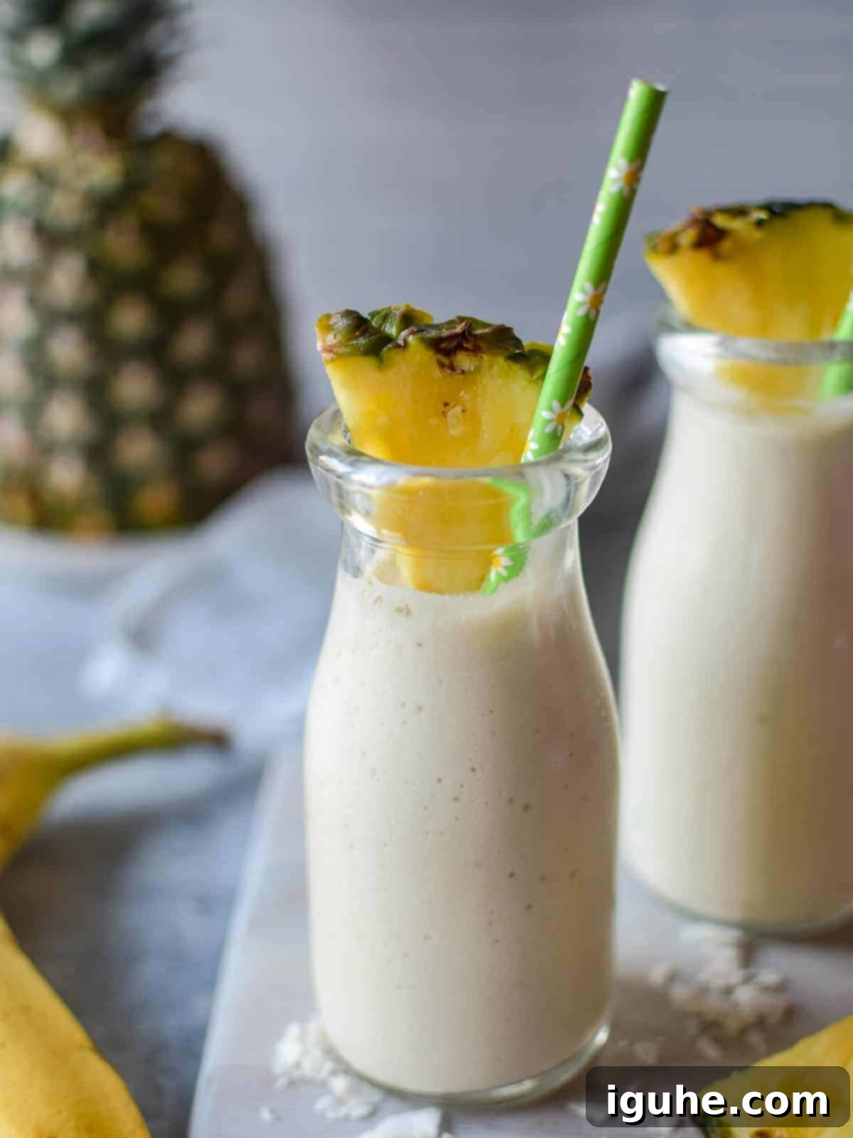 Close-up of a vibrant yellow banana and pineapple smoothie in a clear glass with a reusable straw, suggesting freshness and health.