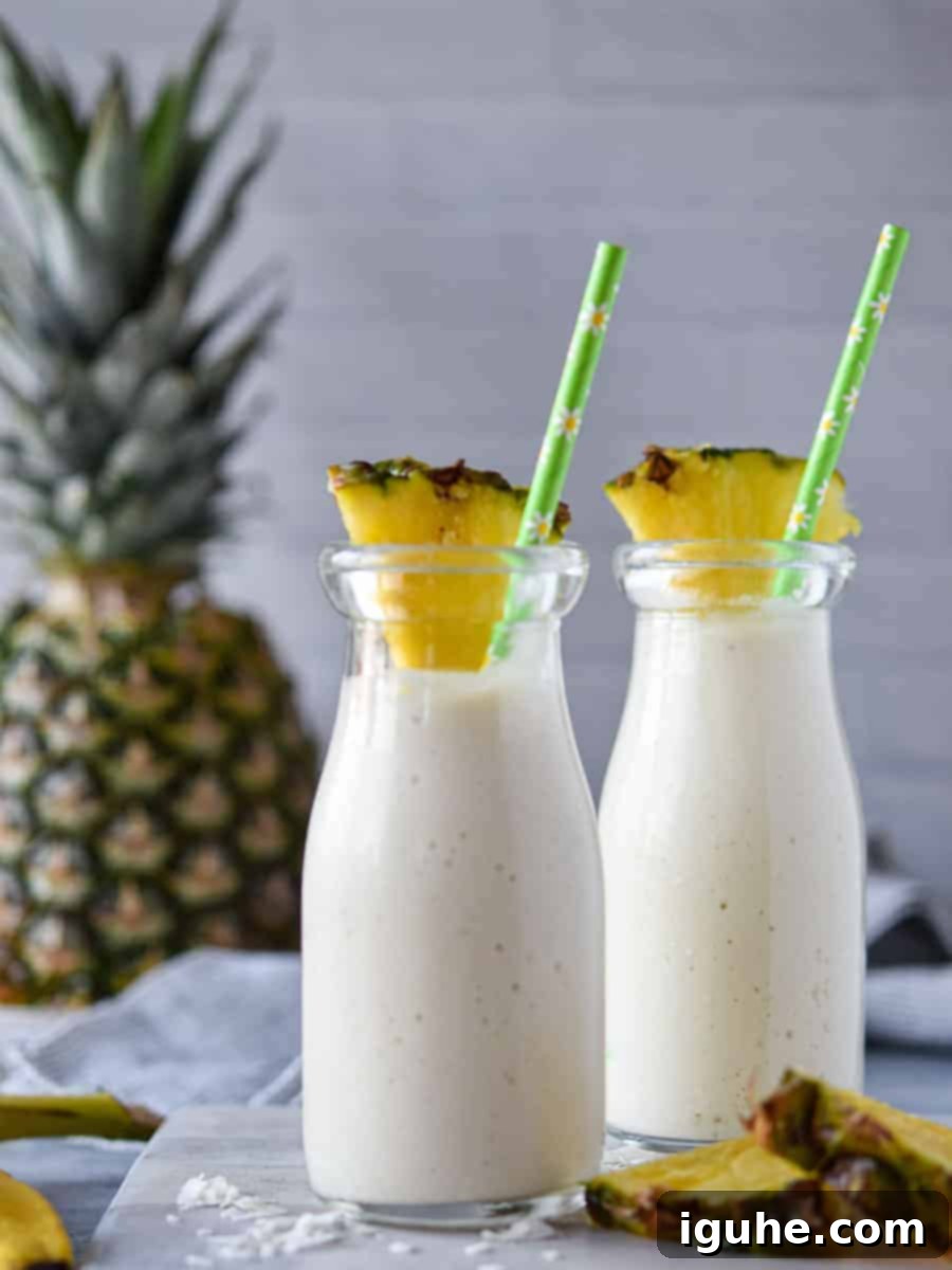Tropical Banana Pineapple Bliss 3 Two glasses of vibrant banana pineapple smoothie with fresh pineapple slices on the side, set against a blurred tropical background.