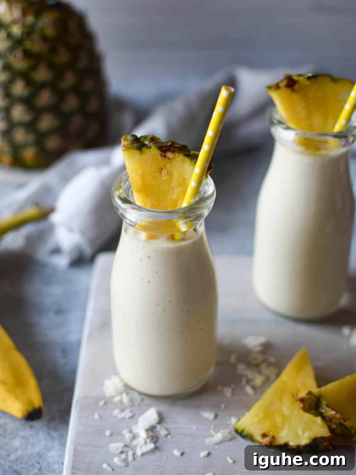 Tropical Banana Pineapple Bliss 4 Close-up of a refreshing banana and pineapple smoothie in a clear glass with a straw, garnished with a tropical flower.