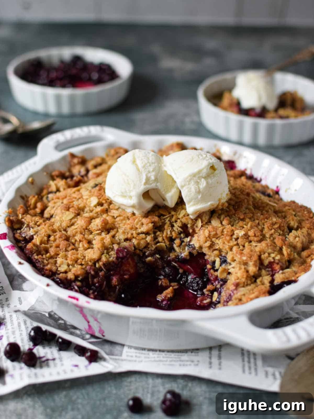 Angled view of blueberry crisp in a white pie plate, golden brown and bubbling.
