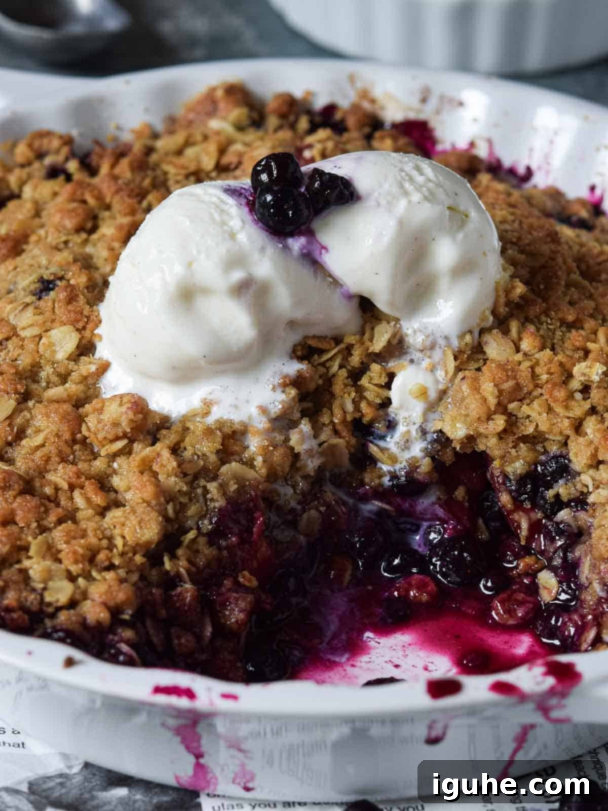 Summer Peach & Wild Blueberry Crumble 8 Close-up of peach blueberry crisp in a white pie plate with melting vanilla ice cream on top.