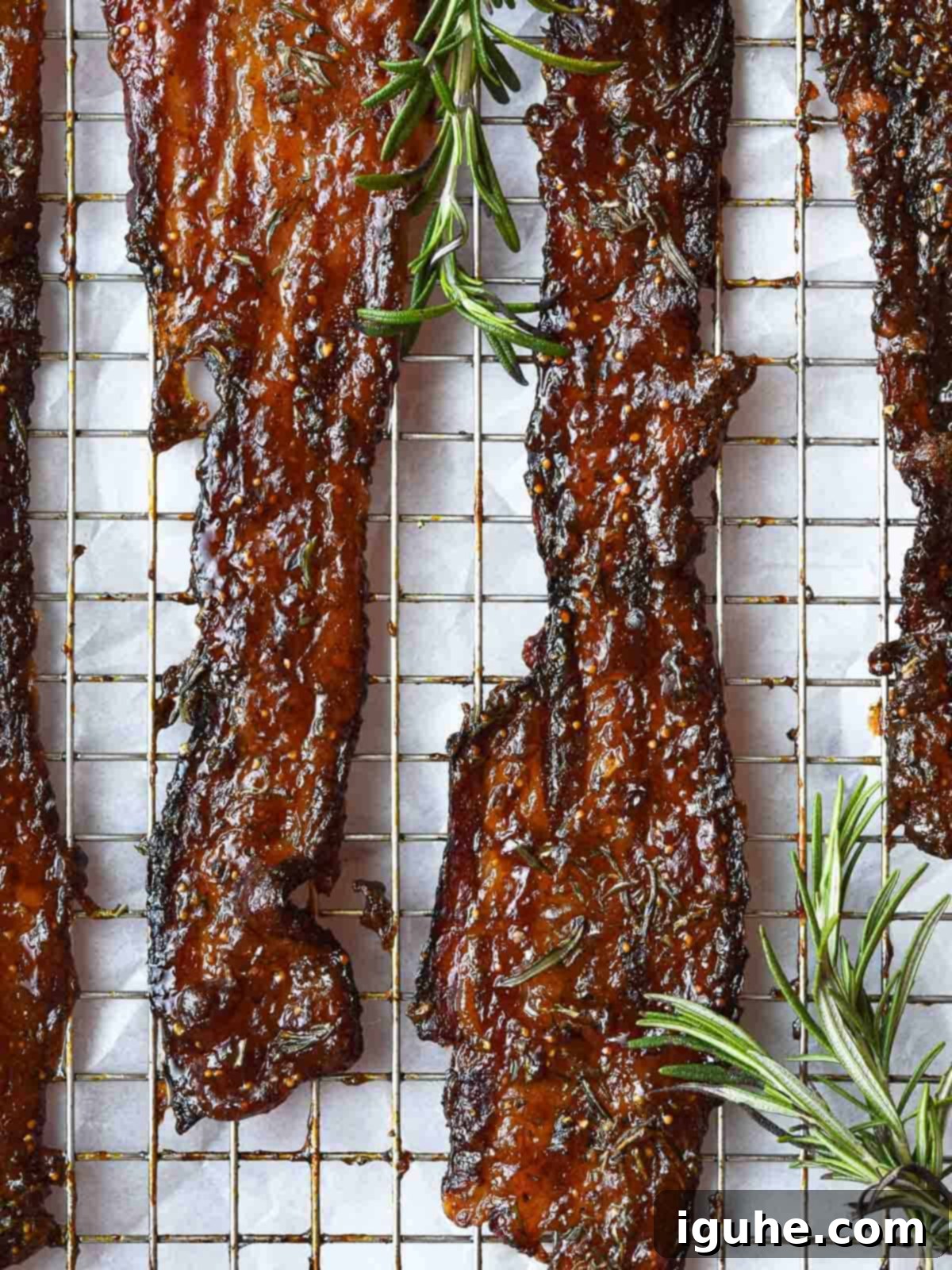 Candied bacon with rosemary on a wire rack, glistening with fig jam.