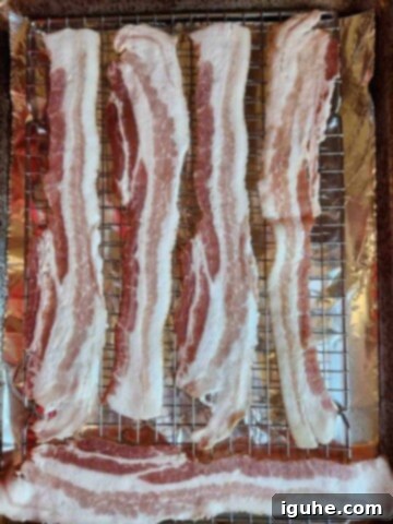 Raw thick-cut bacon strips neatly arranged on a wire rack over a baking sheet.