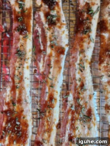 Raw bacon on a baking sheet with fig jam and chopped fresh rosemary on top, ready for the oven.