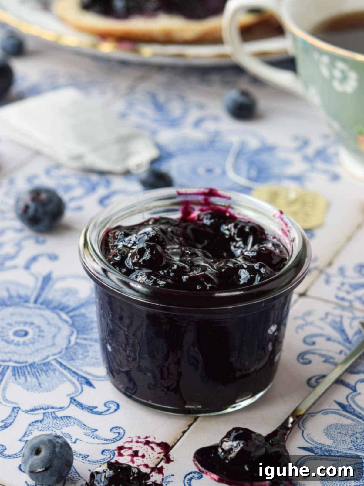 Close-up of blueberry earl grey jam on blue tile in a small glass jar.