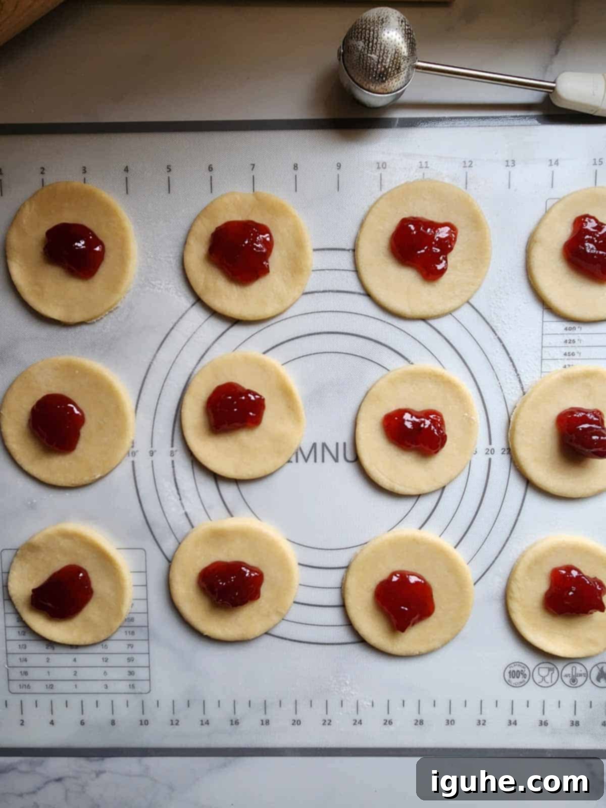 Circular pie dough pieces laid flat on parchment paper, each with a small dollop of vibrant strawberry jam placed precisely in the center, ready for folding and sealing.