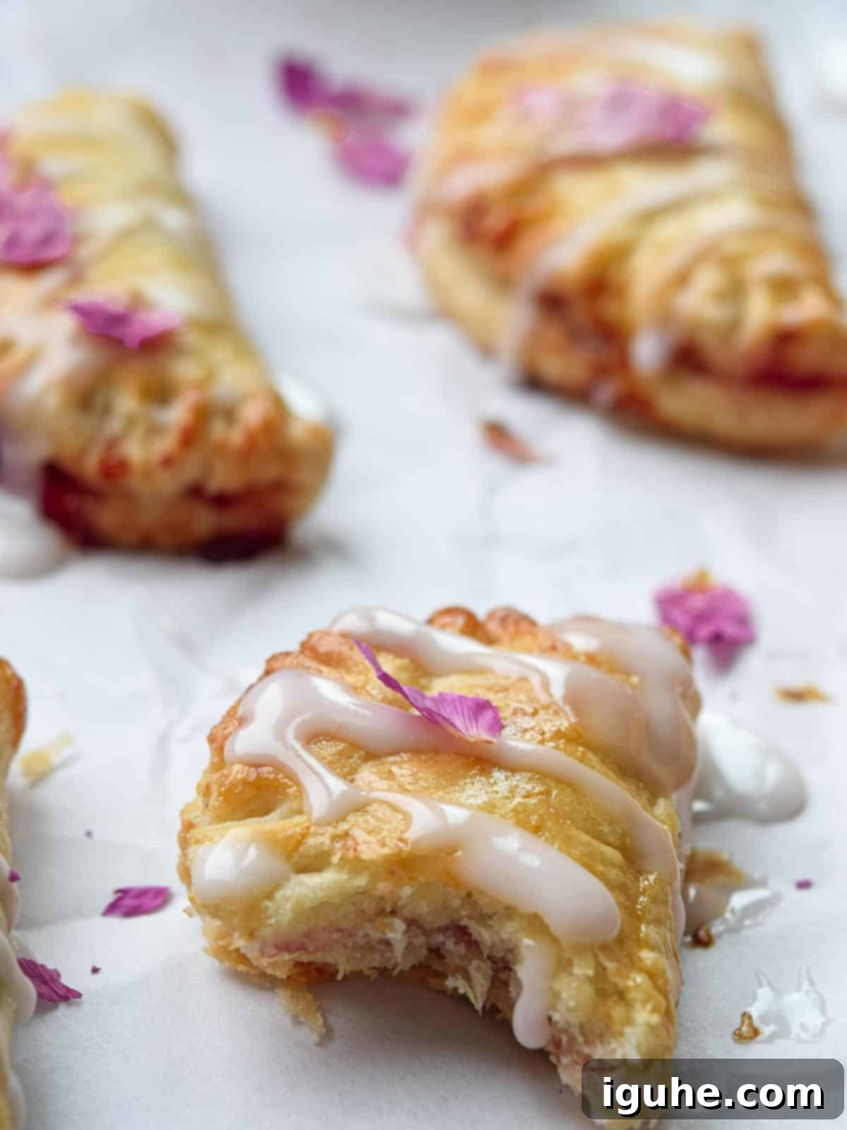A close-up view of a strawberry mini pie with a bite taken out, revealing the sweet strawberry jam filling and flaky crust, resting on white parchment paper.