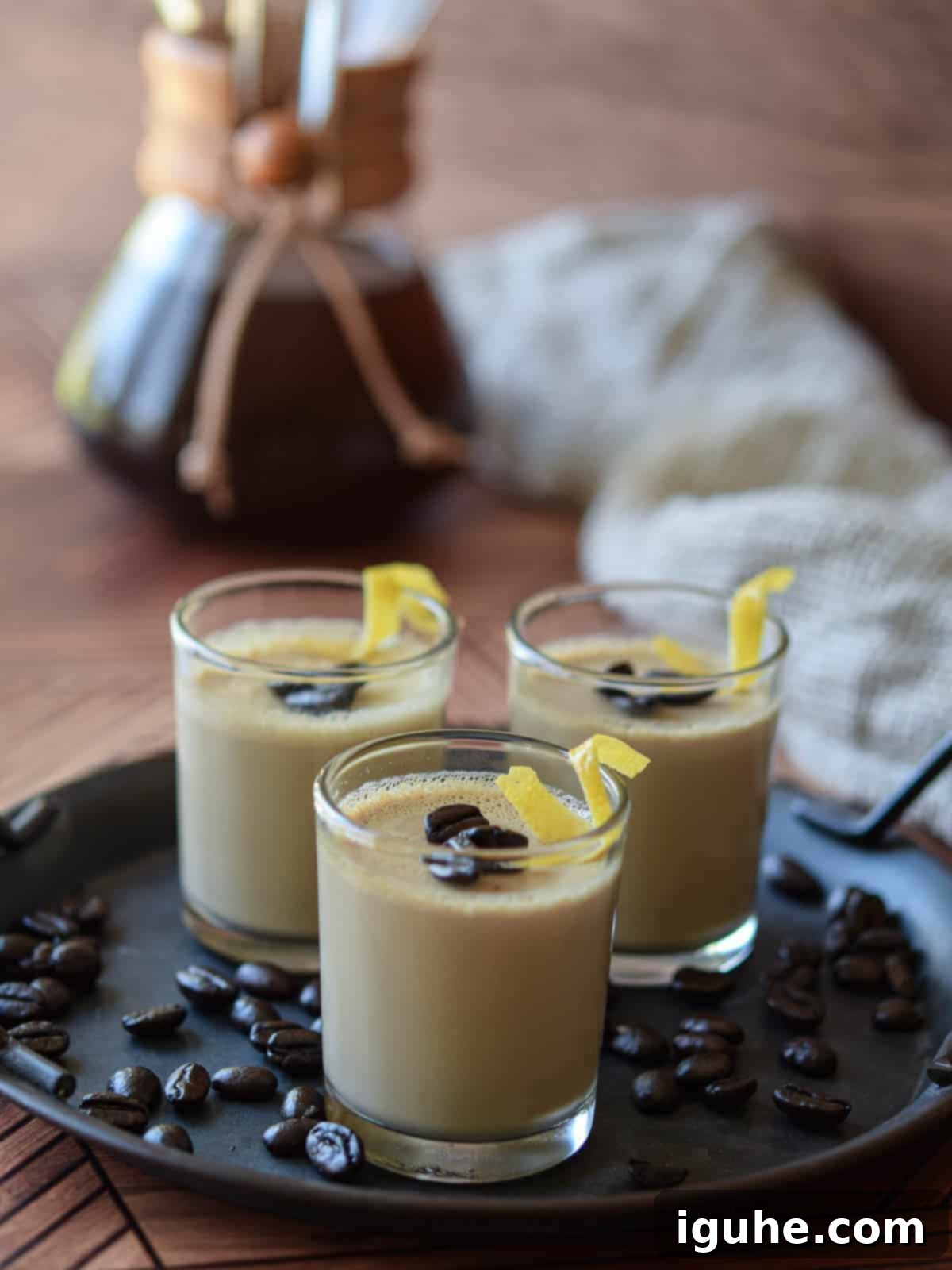 Espresso panna cotta served in small clear glass jars, garnished with whole coffee beans and elegant lemon rind twists, suggesting a sophisticated dessert.