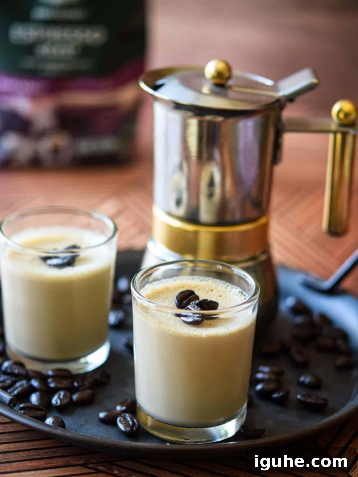 Velvet Espresso Panna Cotta 8 Two small glass jars of espresso panna cotta, garnished with coffee beans and lemon rind, are artfully arranged in the foreground with a blurred coffee machine in the background, suggesting a delightful coffee-themed dessert.