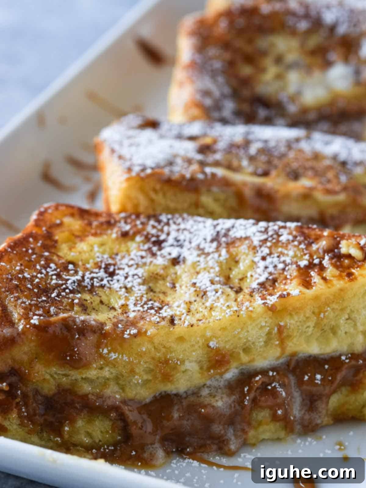 Decadent Biscoff Stuffed French Toast 3 Close-up, angled view of prepared Biscoff and cream cheese stuffed French toast slices on a white plate, ready to be cooked.