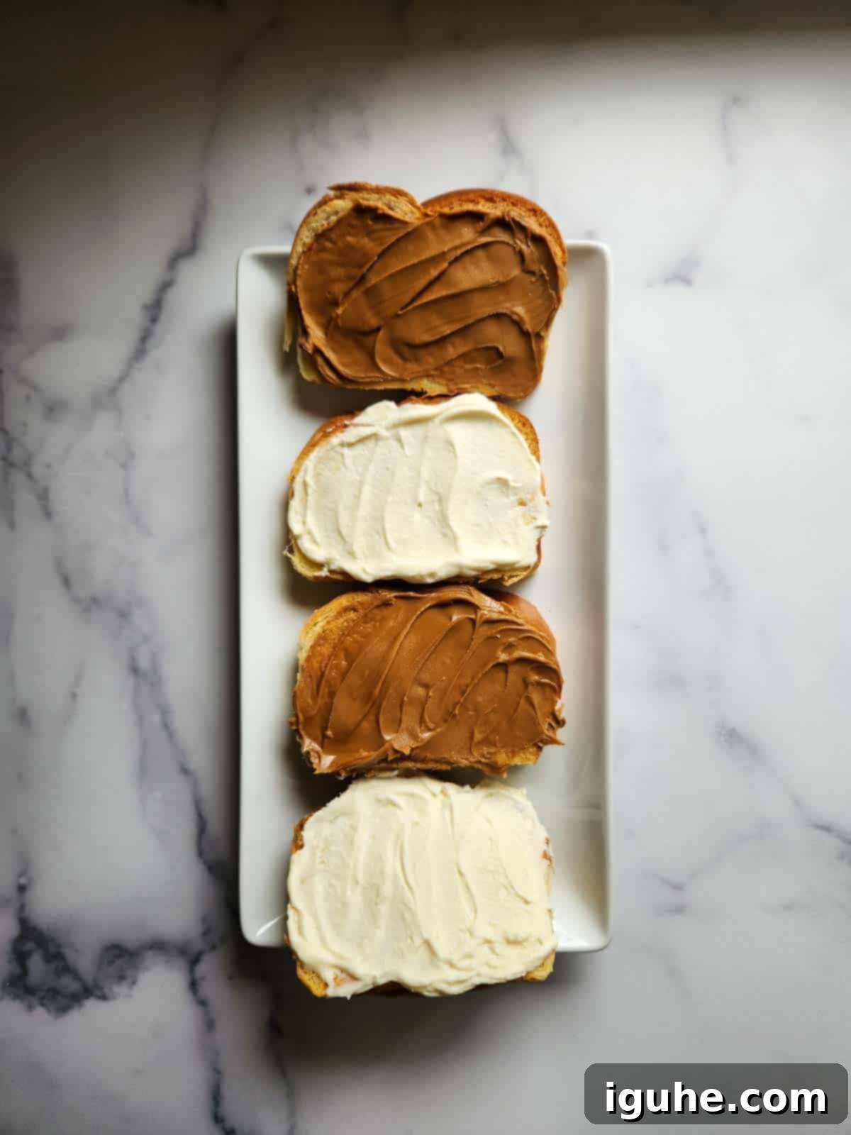 Decadent Biscoff Stuffed French Toast 4 Four slices of thick bread, two spread with Biscoff cookie butter and two with cream cheese, ready to be combined into sandwiches.