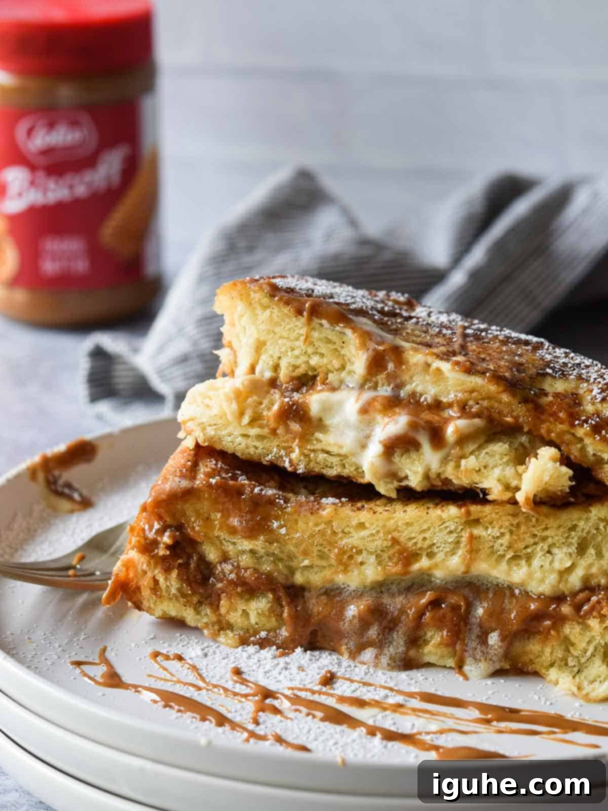 Decadent Biscoff Stuffed French Toast 6 A slice of Biscoff Stuffed French Toast, cut open to reveal the melted cookie butter and cream cheese filling, on a white plate with a fork.