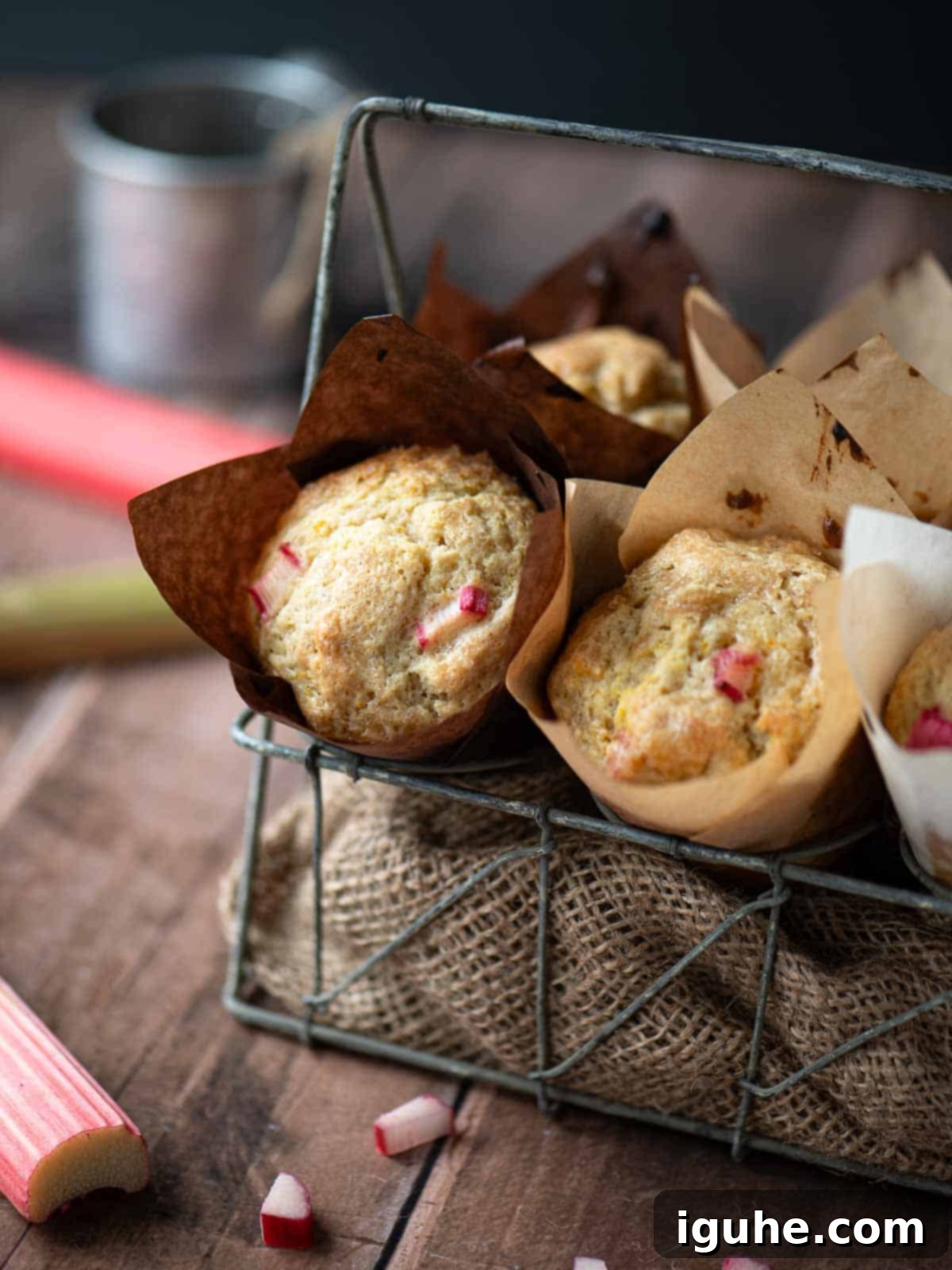 Rhubarb muffins in a metal basket with stalks of rhubarb to the side.