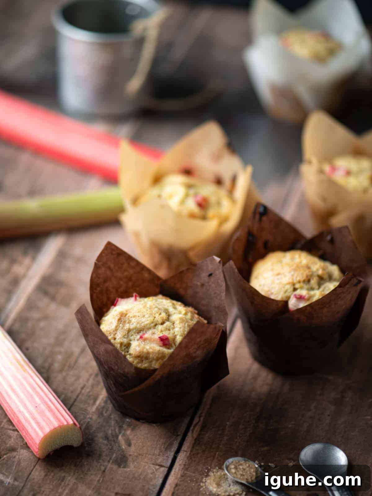 Tangy Rhubarb Muffins 8 Five rhubarb muffins on a wooden surface with rhubarb stalks next to it.