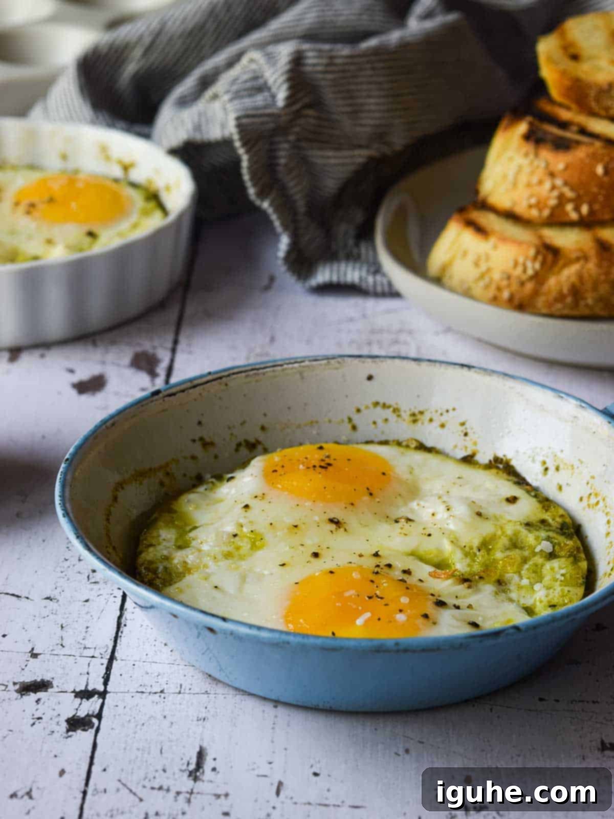 Pesto baked eggs in a blue skillet on a white surface.
