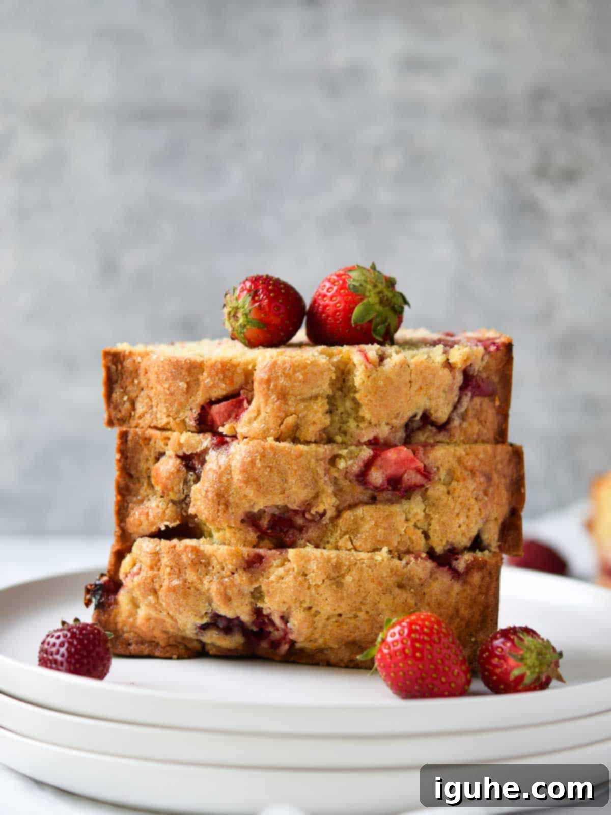Strawberry bread sliced and stacked on a white plate, showcasing its moist texture and fresh berry pieces.