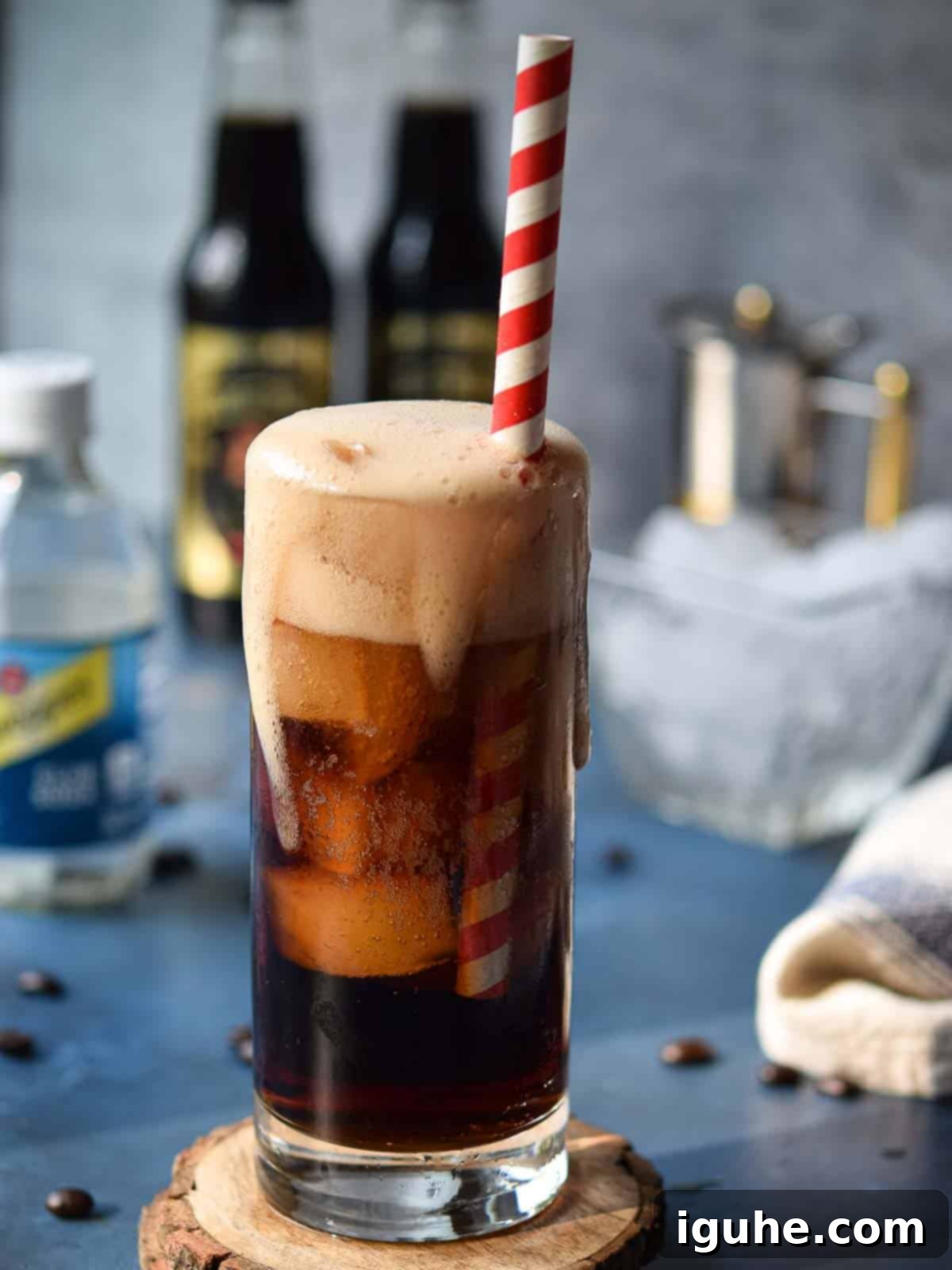 Espresso soda in a glass just poured with foam dripping down, resting on a light surface.