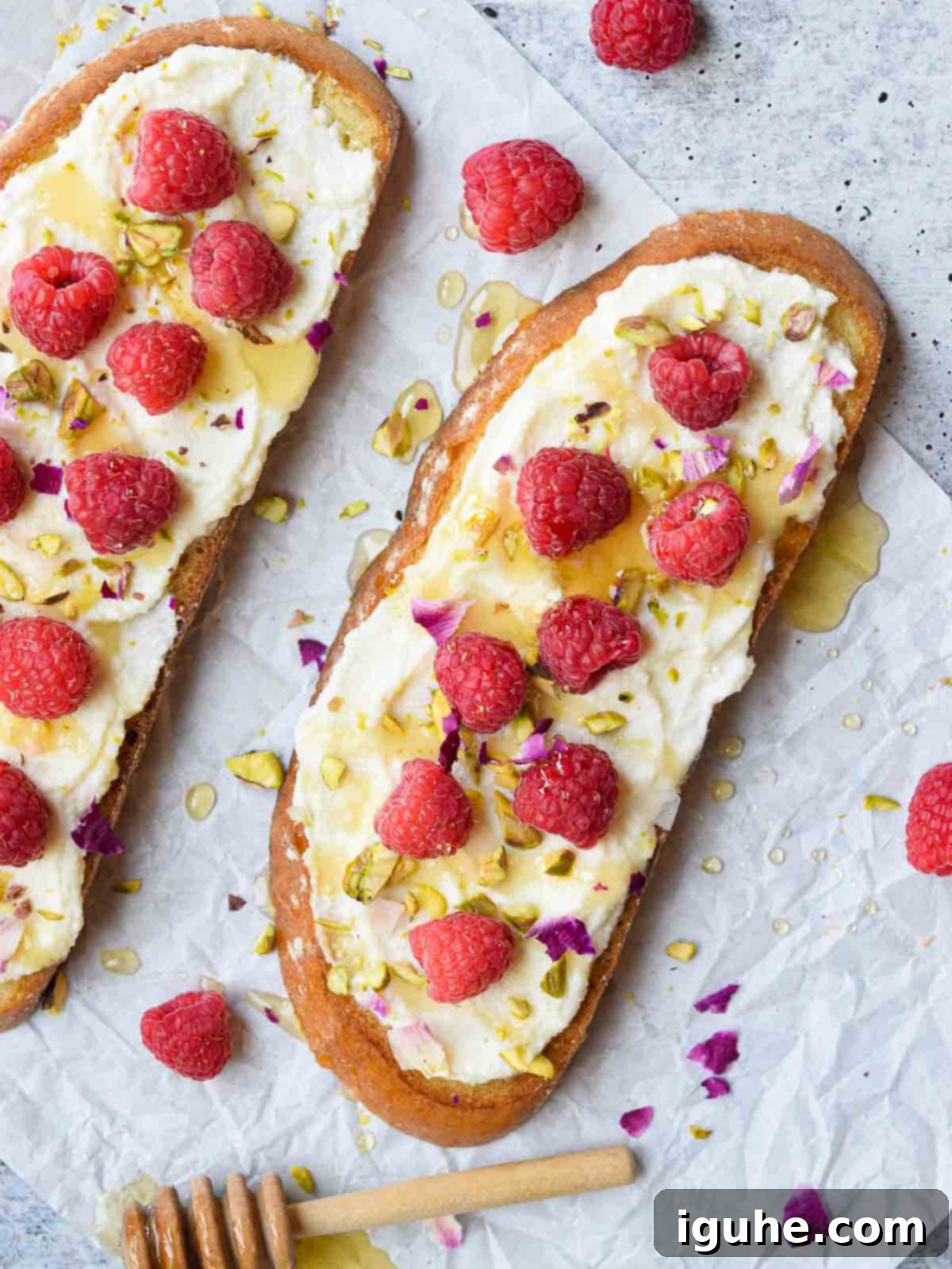 Overhead and close-up view of elegant lemon ricotta raspberry toast on a concrete surface, adorned with edible flowers.