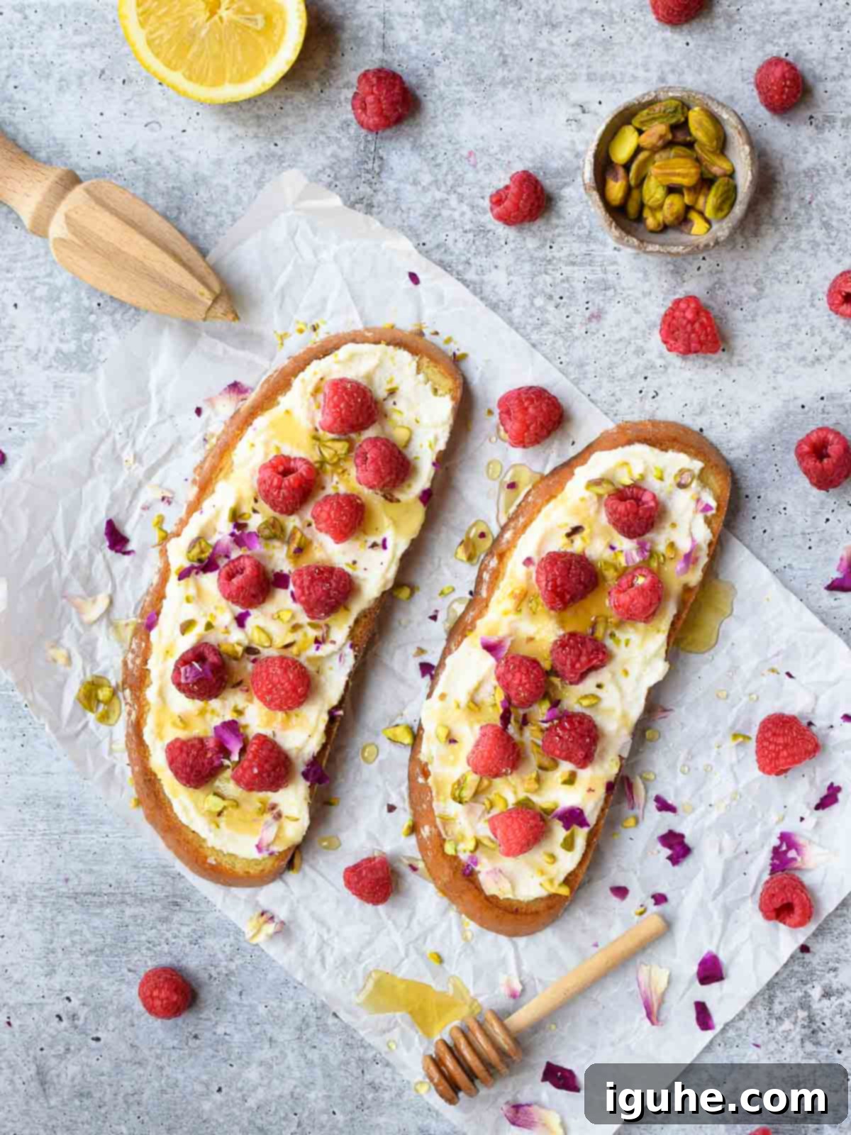 Bright Lemon Raspberry Ricotta Toast 3 Overhead view of two slices of raspberry toast on white parchment paper on a grey surface, ready for delicious toppings.