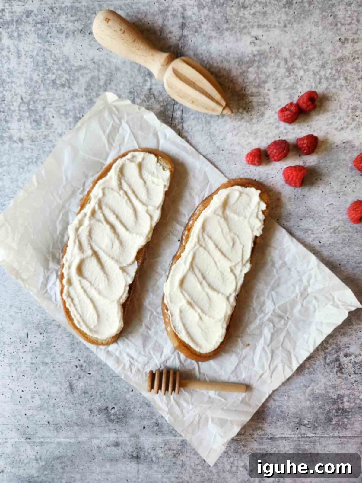 Bright Lemon Raspberry Ricotta Toast 5 Two slices of toast with a creamy lemon ricotta spread on parchment paper, with fresh raspberries on the side.