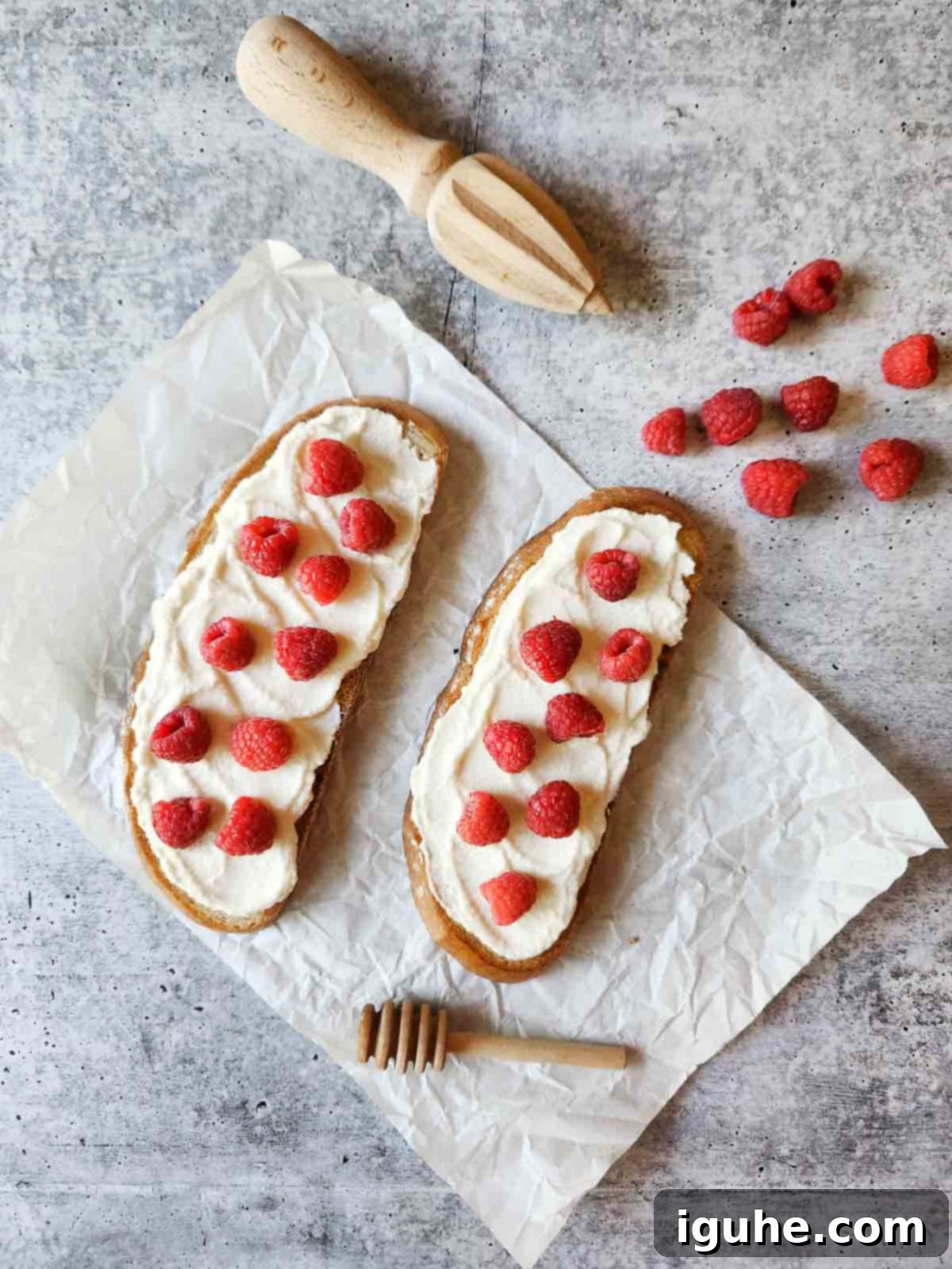 Bright Lemon Raspberry Ricotta Toast 6 Two slices of toast with a creamy ricotta base and fresh raspberries carefully arranged on white parchment paper.