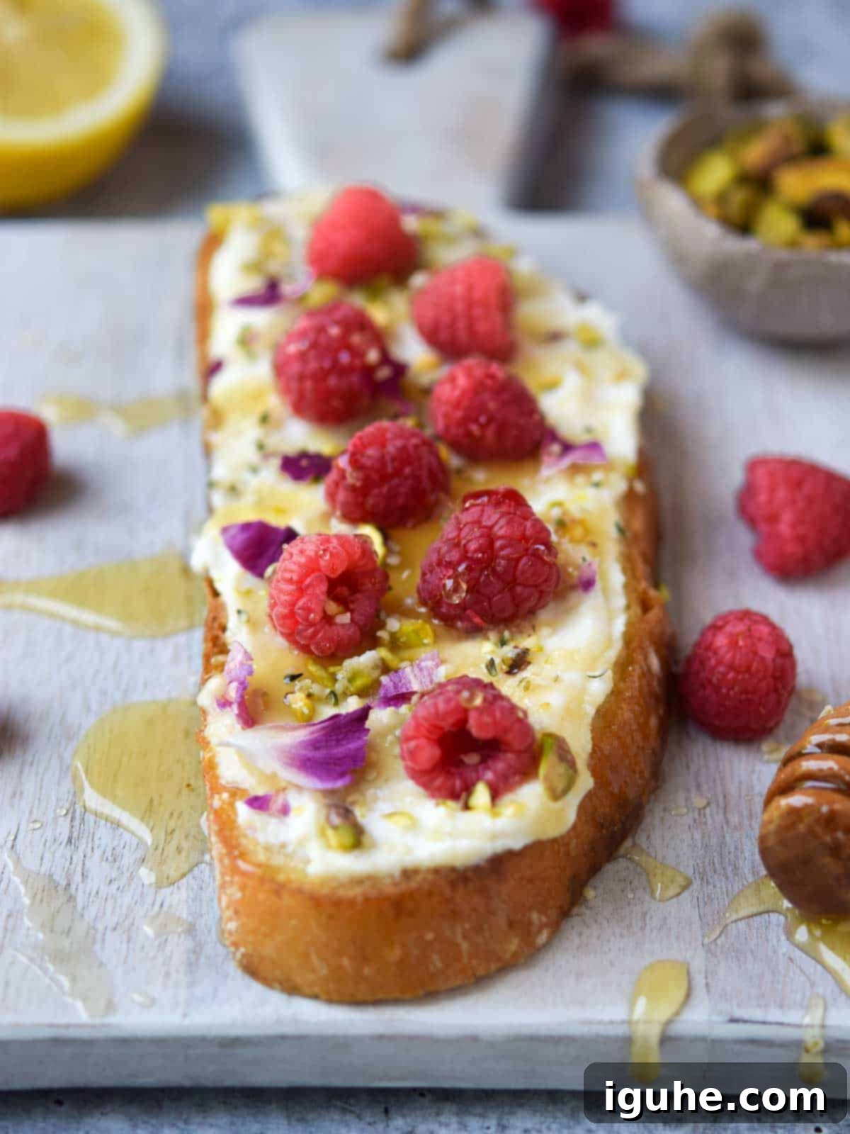 Bright Lemon Raspberry Ricotta Toast 8 Lemon ricotta raspberry toast with honey drizzled over it, presented beautifully on a grey cutting board.