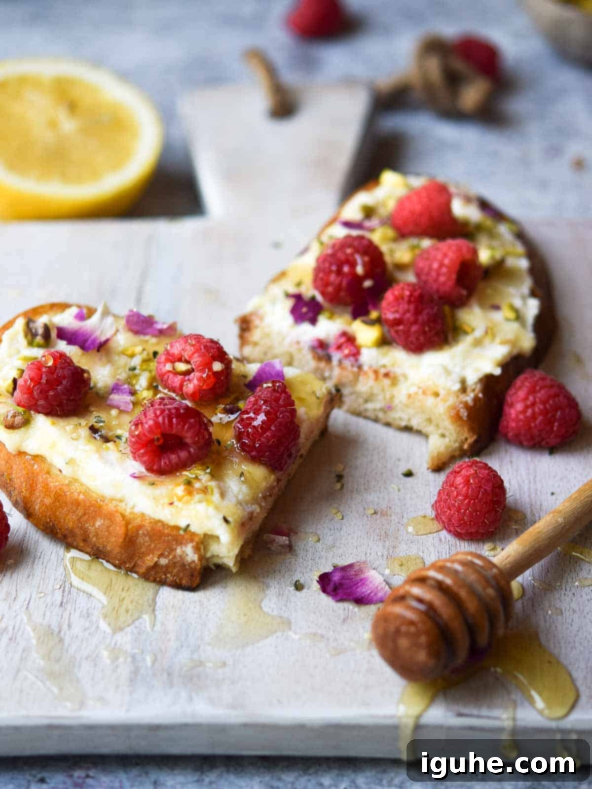 Bright Lemon Raspberry Ricotta Toast 9 A delectable slice of raspberry toast, elegantly cut in half, with honey dripping tantalizingly down a wooden cutting board, inviting a taste.