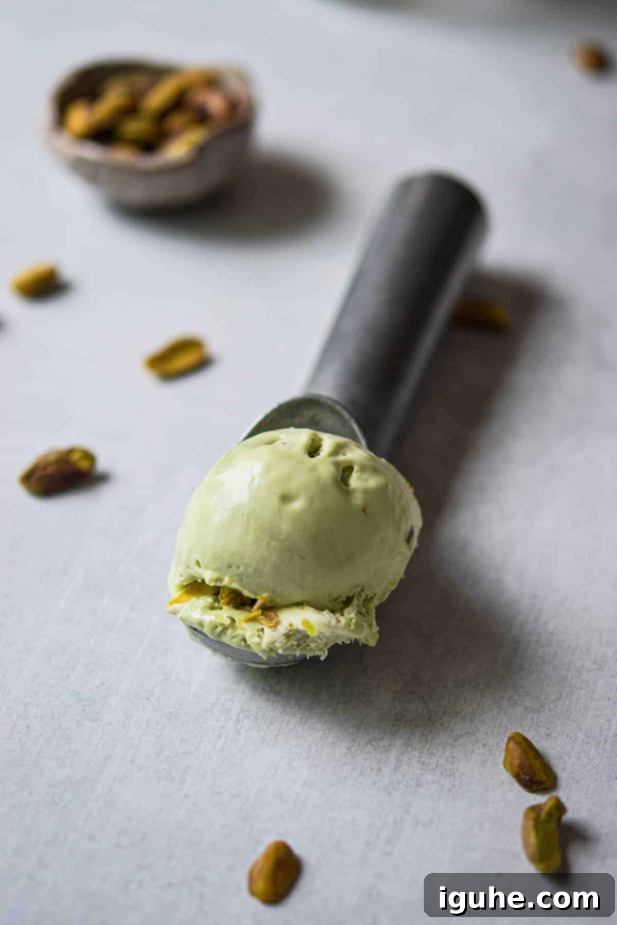 Effortless Pistachio Ice Cream 3 A perfectly scooped ball of rich pistachio ice cream on a metal ice cream scoop, highlighting its creamy texture.