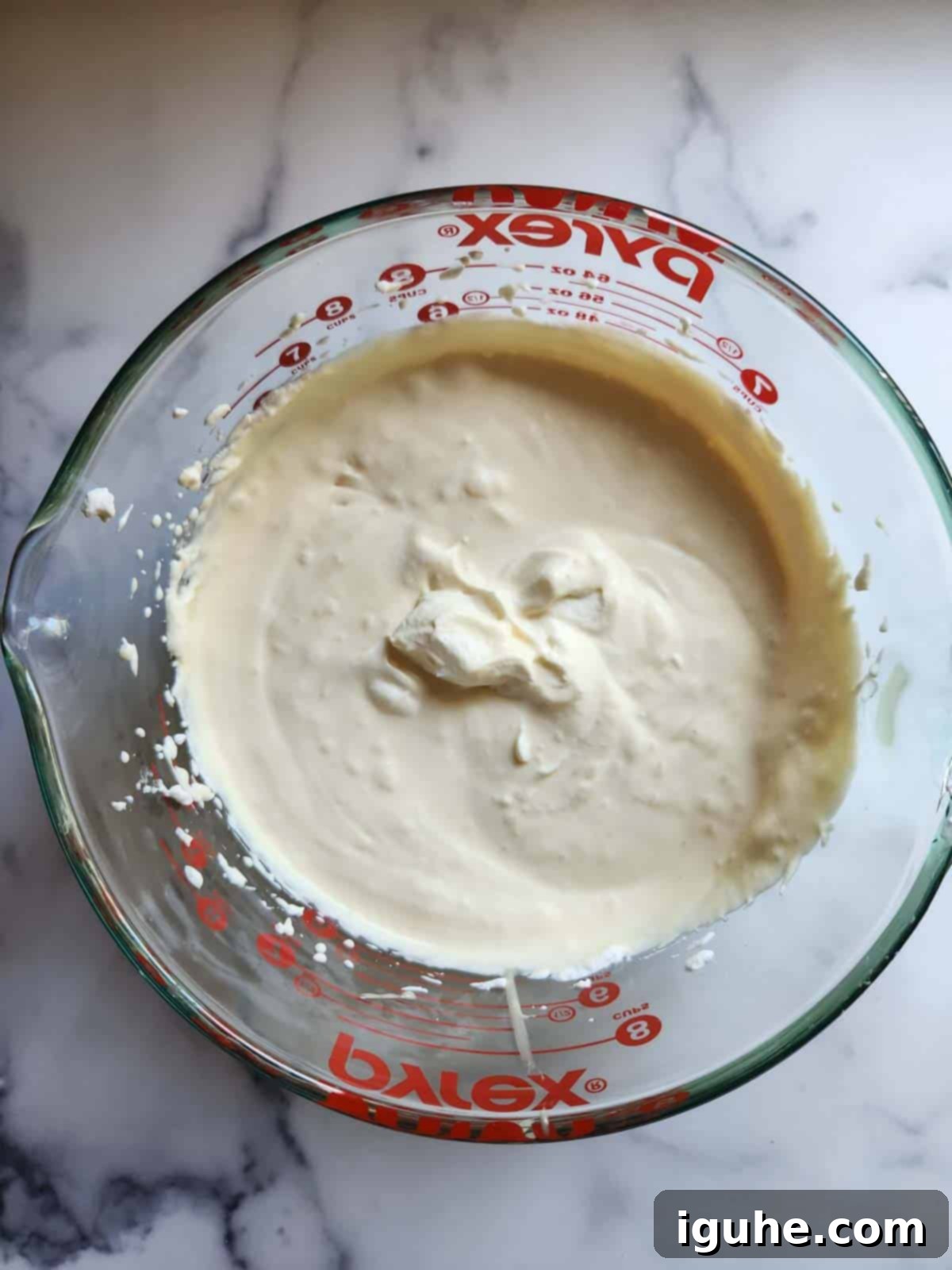 Effortless Pistachio Ice Cream 5 Whipped heavy cream combined with sweetened condensed milk in a clear glass bowl, ready for the next step.