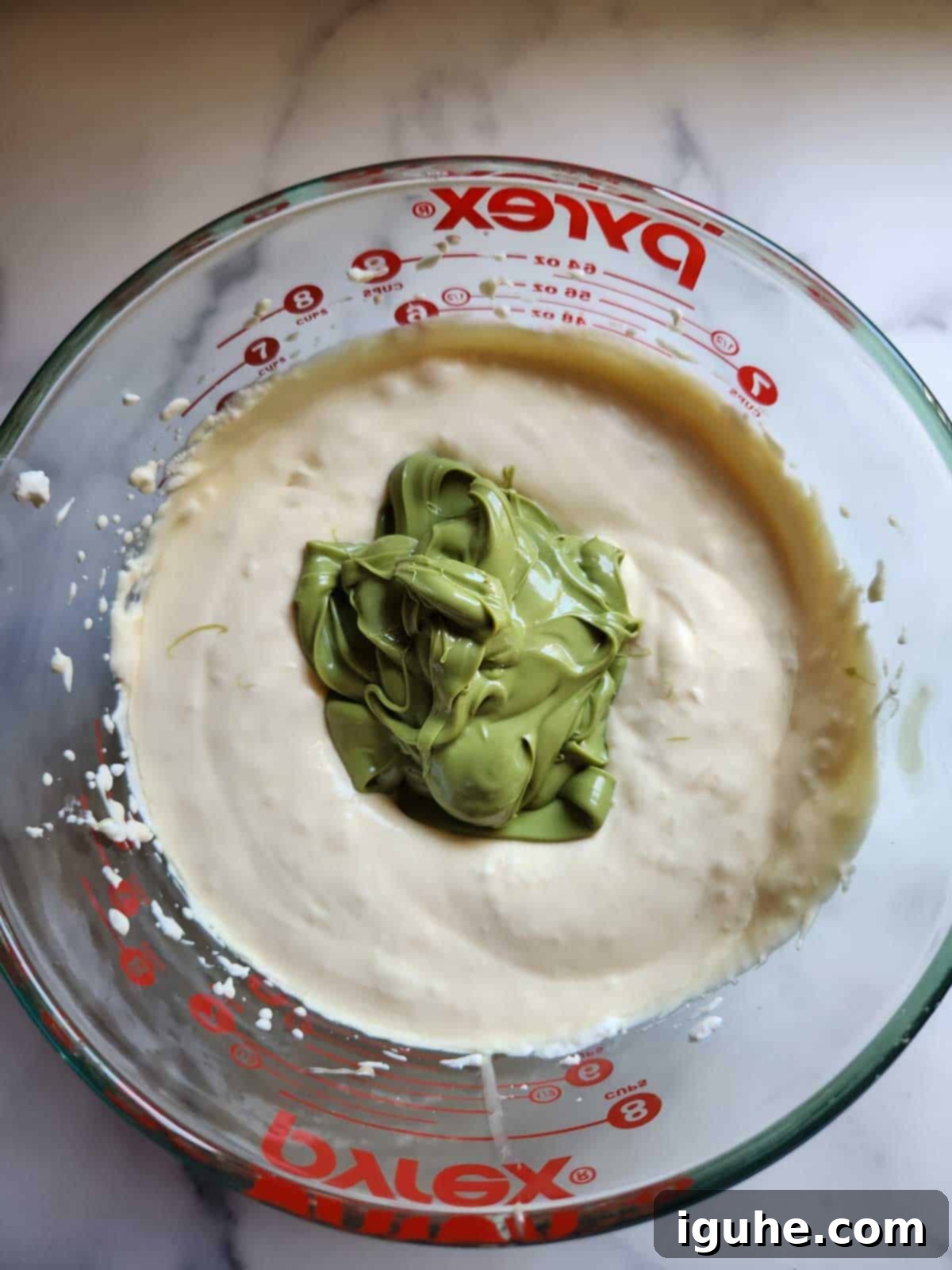 Effortless Pistachio Ice Cream 6 Pistachio paste being mixed into the whipped cream and condensed milk, beginning to turn the mixture green.