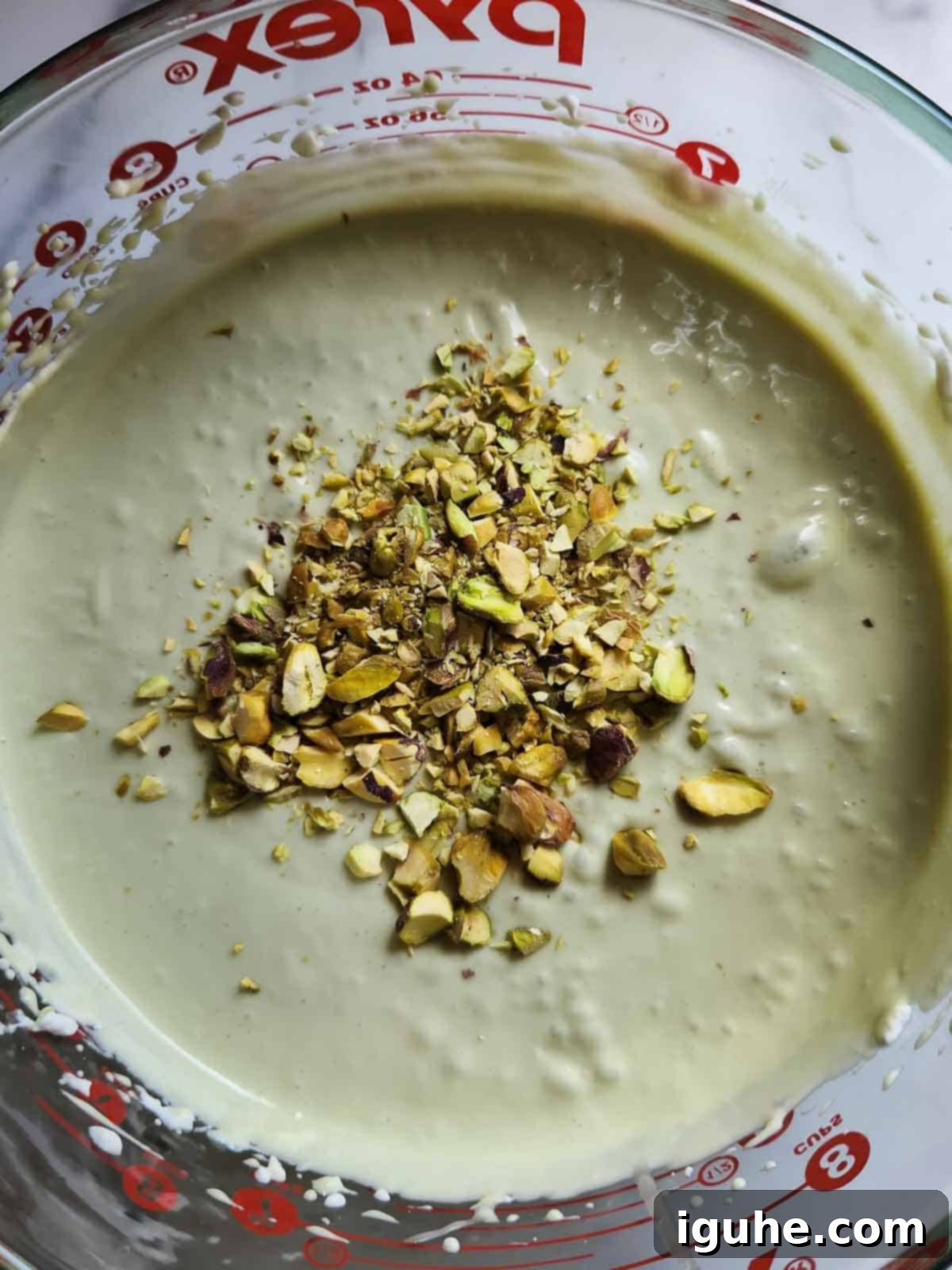 Effortless Pistachio Ice Cream 7 The fully mixed pistachio ice cream base, showing its creamy texture and light green color, with chopped pistachios visible.