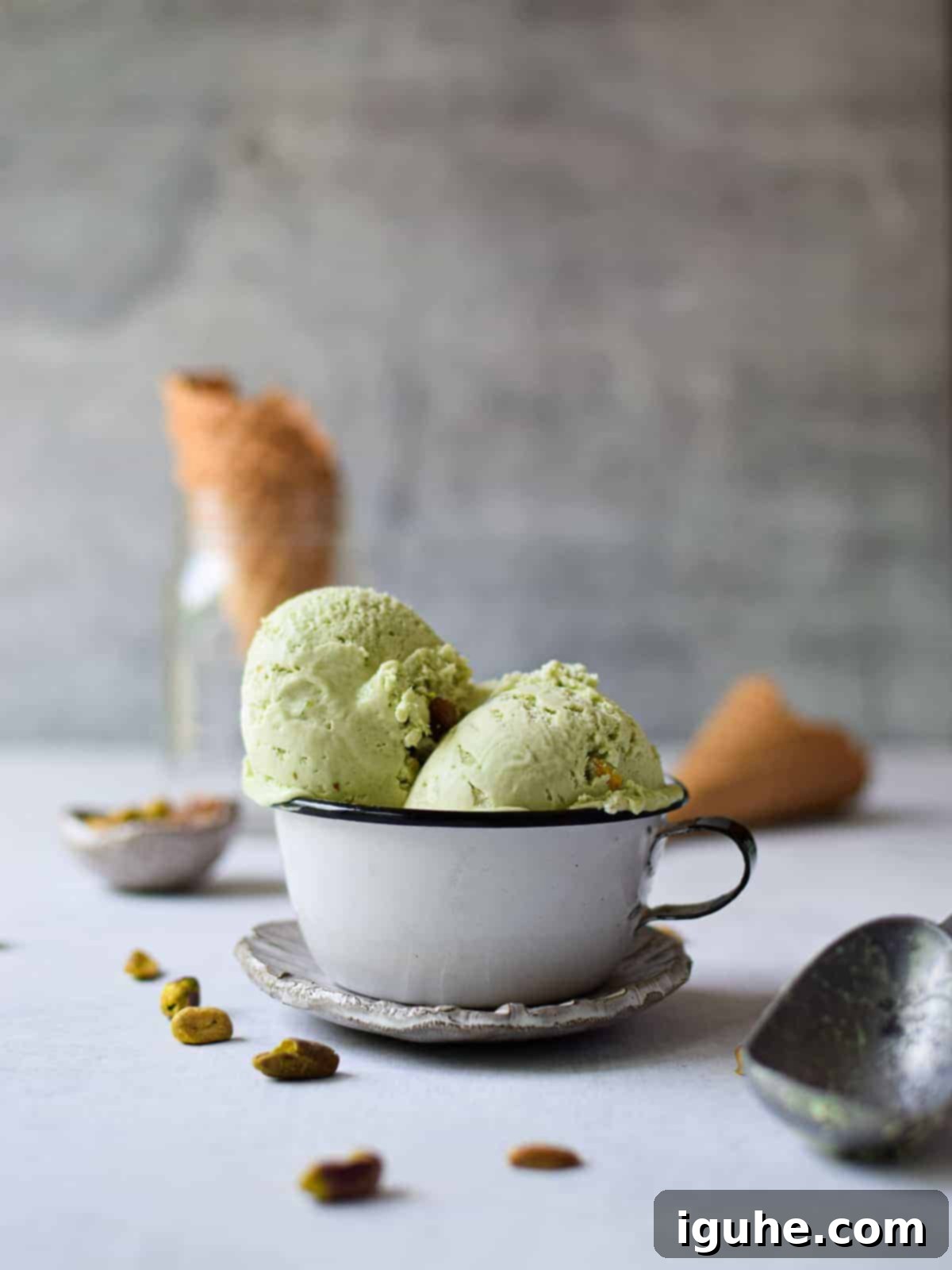 Effortless Pistachio Ice Cream 8 Close-up, eye-level shot of two scoops of vibrant green pistachio ice cream in a white bowl, showcasing its smooth texture.
