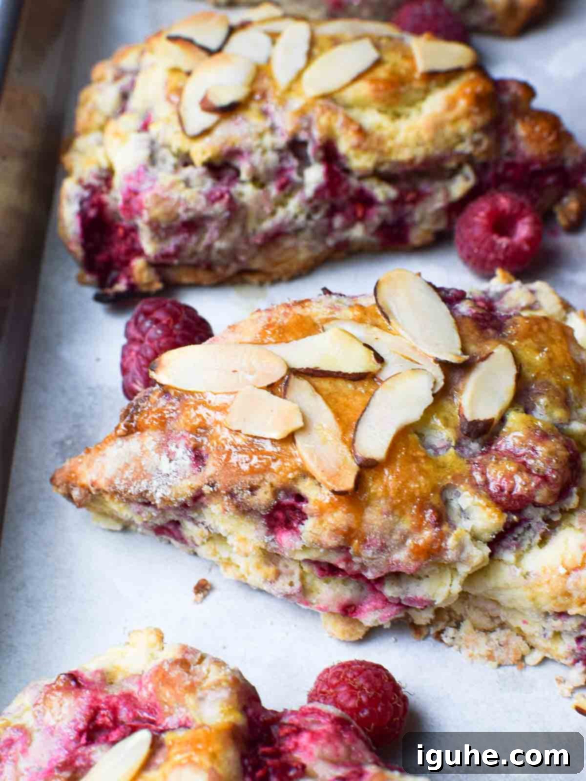 Buttery Raspberry Almond Scones 3 Close-up of freshly baked raspberry almond scones cooling on parchment paper.