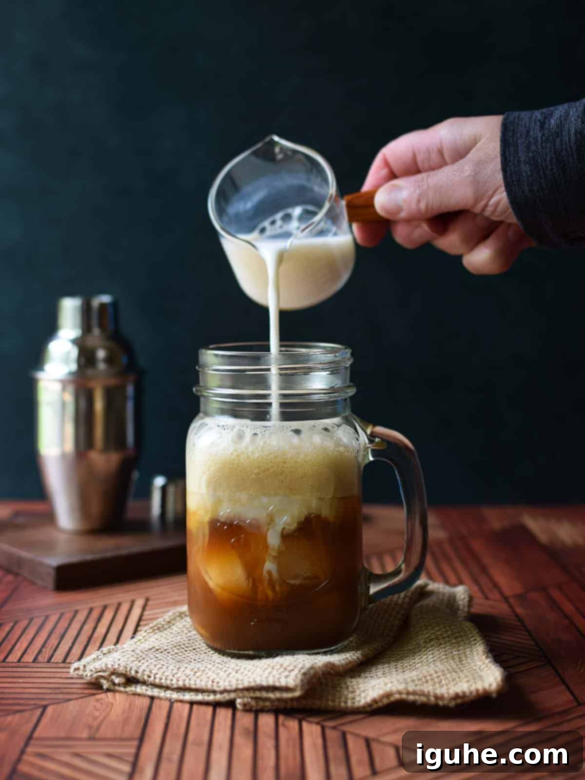 Creamy milk being poured into a clear glass mug filled with frothy brown sugar shaken chai tea and ice.