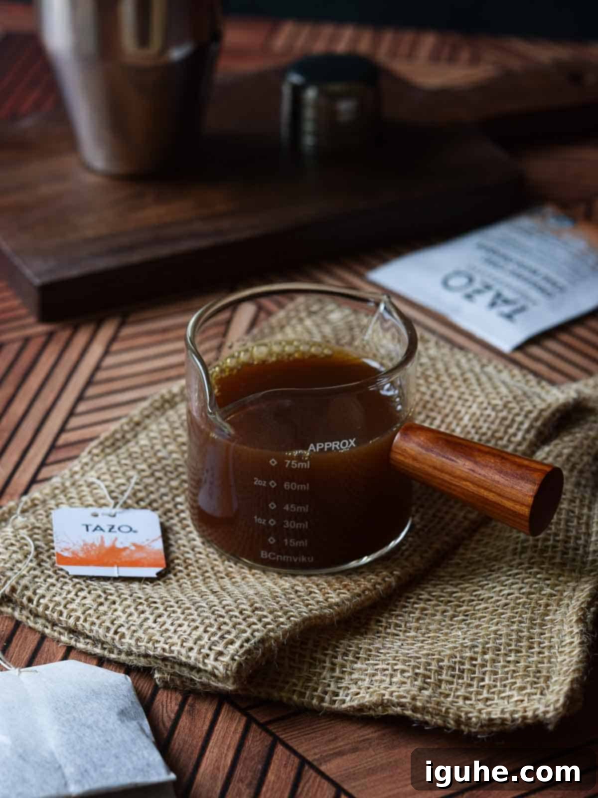 Caramel-Kissed Shaken Chai 3 A measuring cup filled with rich, dark chai concentrate sitting on a rustic brown wooden surface.