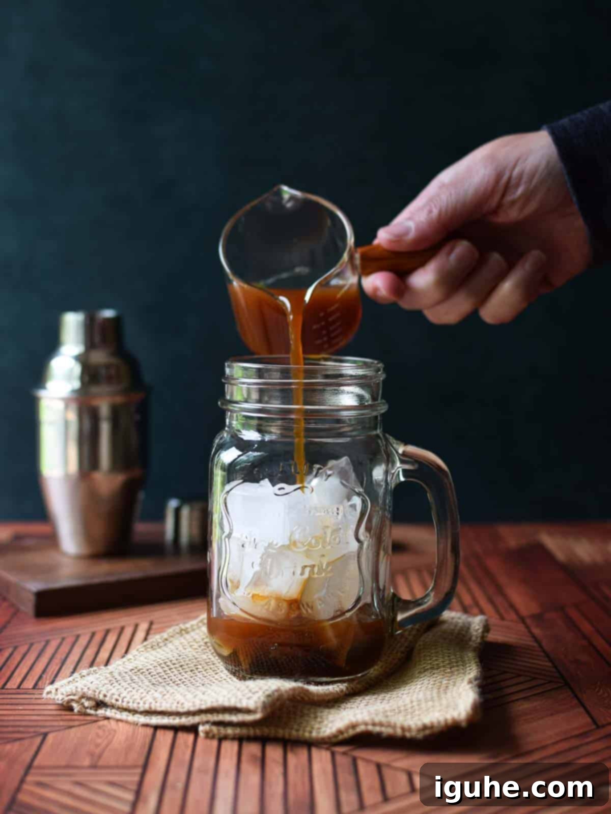 Caramel-Kissed Shaken Chai 4 Rich, dark chai concentrate being poured from a small pitcher into a clear glass mug filled with ice.