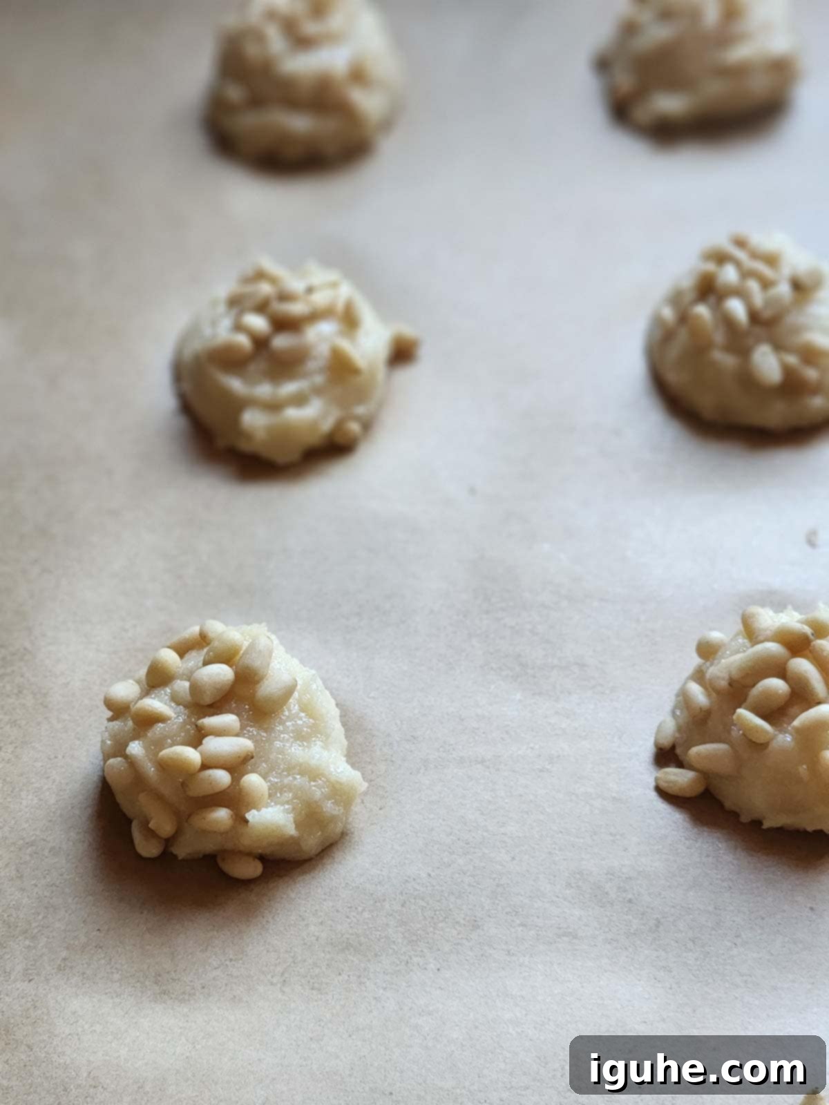 The Easiest Italian Pignoli Cookies 6 Scoops of cookie batter with pine nuts on parchment paper.