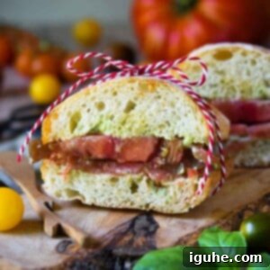Sun-Kissed Heirloom Tomato & Pesto Aioli Sandwich 10 Heirloom tomato sandwich cut open on a wooden board with a red and white string holding it together.