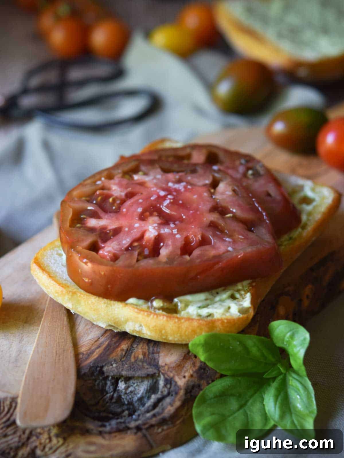 Sun-Kissed Heirloom Tomato & Pesto Aioli Sandwich 7 Sliced red tomatoes on bread with pesto mayo on a wood board.