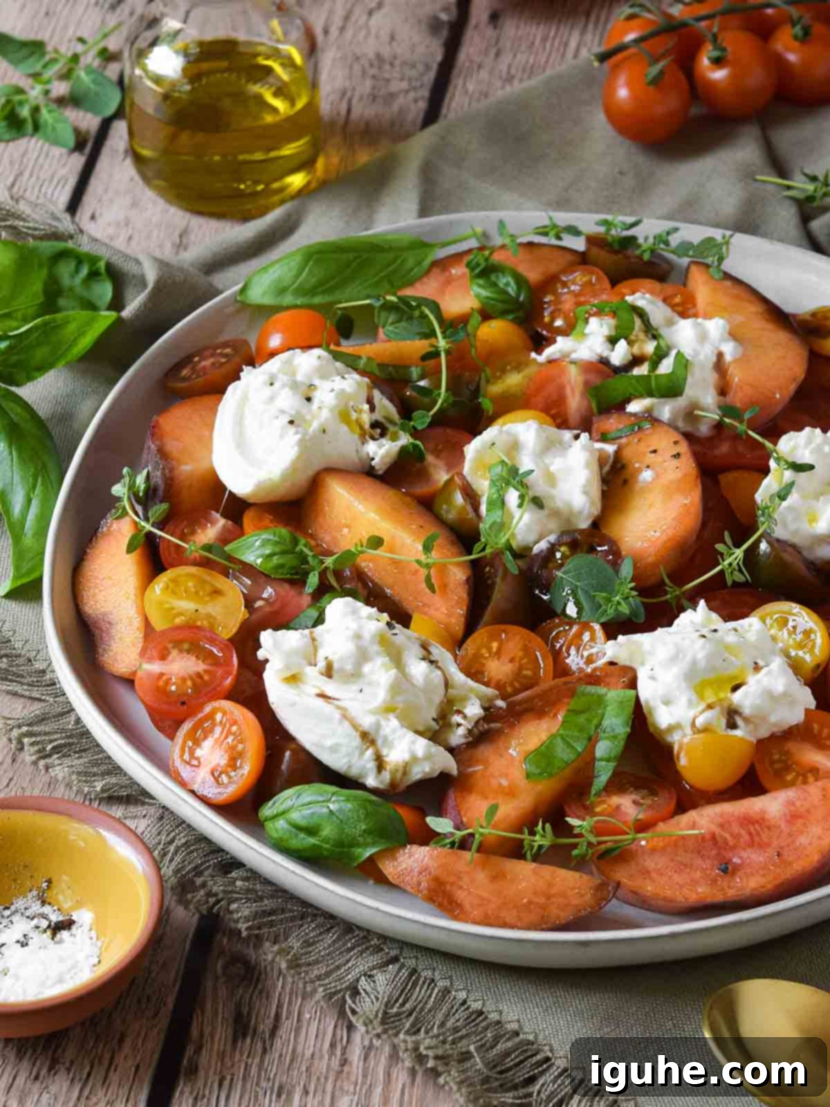 Freshly prepared Burrata Caprese Salad with Peaches, showing vibrant red tomatoes, golden peach slices, and creamy white burrata cheese on a platter.