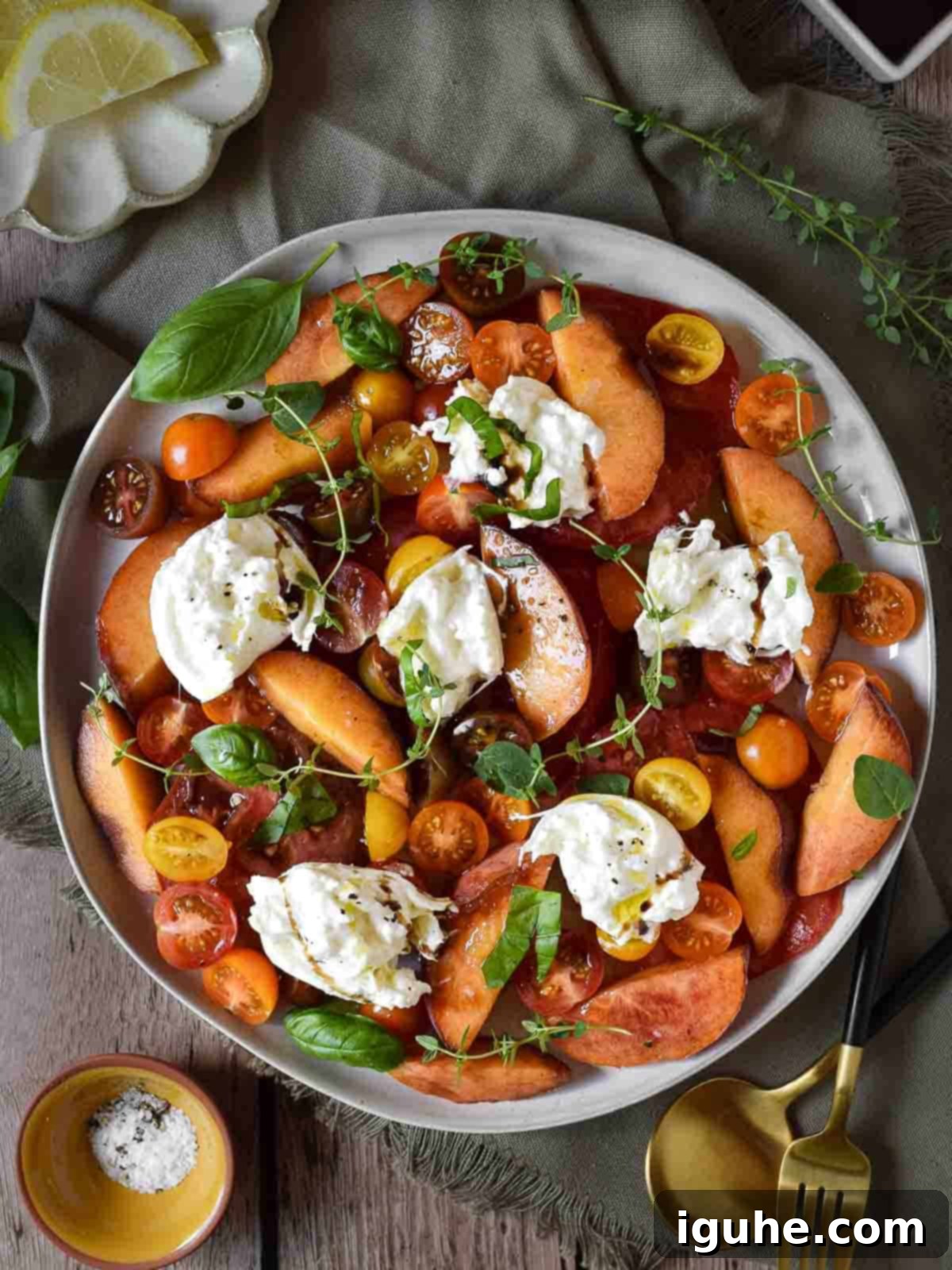 Peaches and Cream Burrata Caprese 3 Overhead view of a vibrant peach, tomato, and burrata salad on a white plate over a rustic wooden surface, highlighting the fresh ingredients.