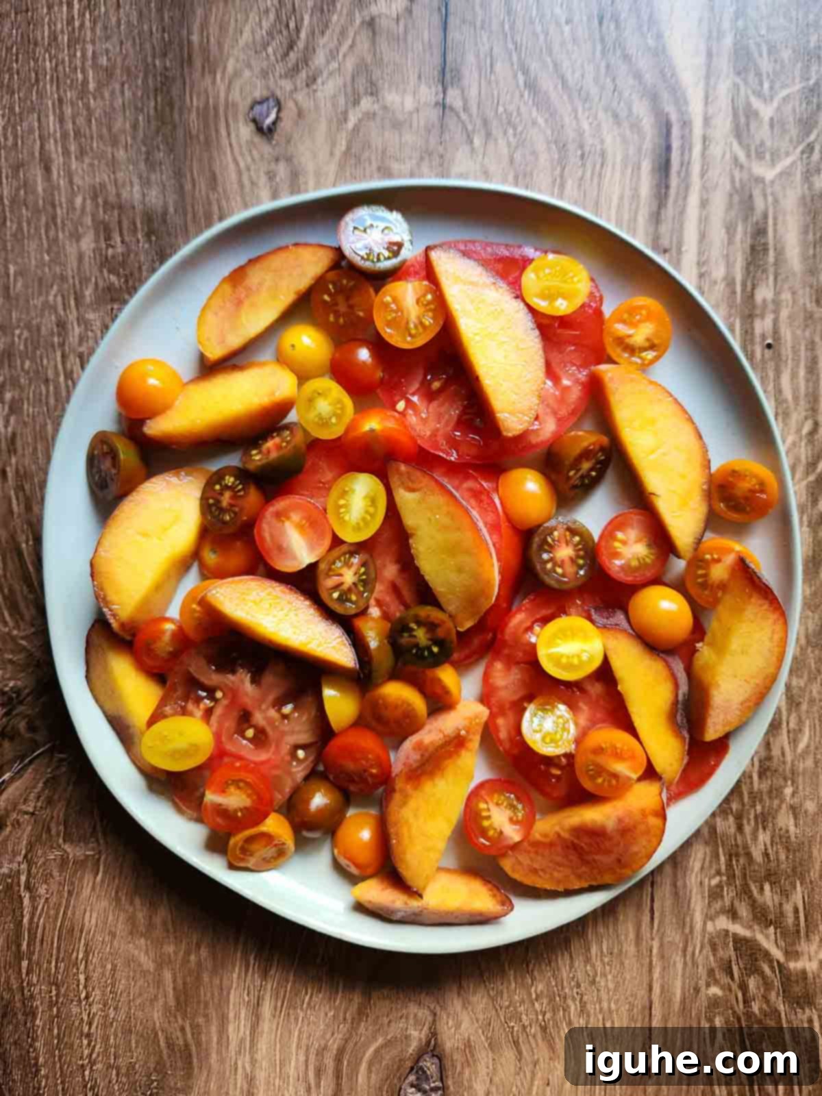 Peaches and Cream Burrata Caprese 5 Sliced tomatoes and peaches artfully arranged on a round white salad plate, ready for the next step of salad assembly.