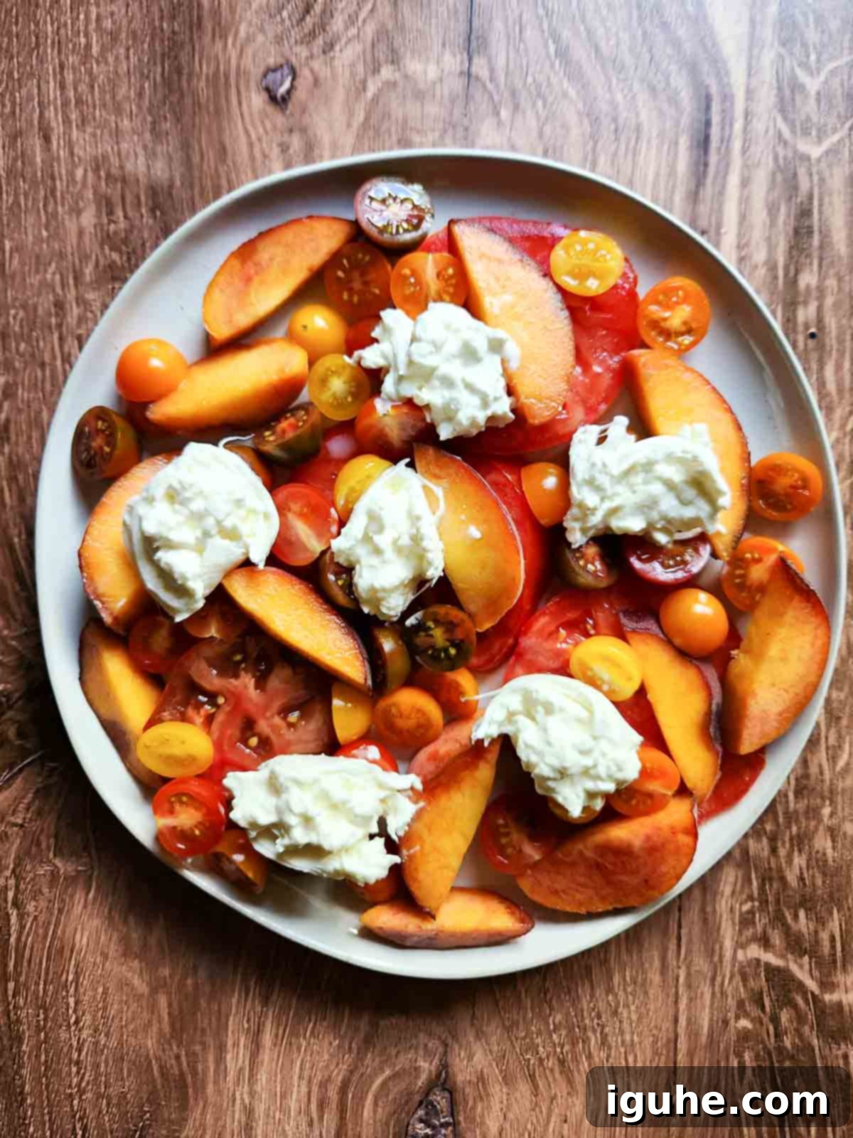 Peaches and Cream Burrata Caprese 6 Tomatoes, peaches, and torn burrata cheese arranged beautifully on a round plate, ready for seasoning.