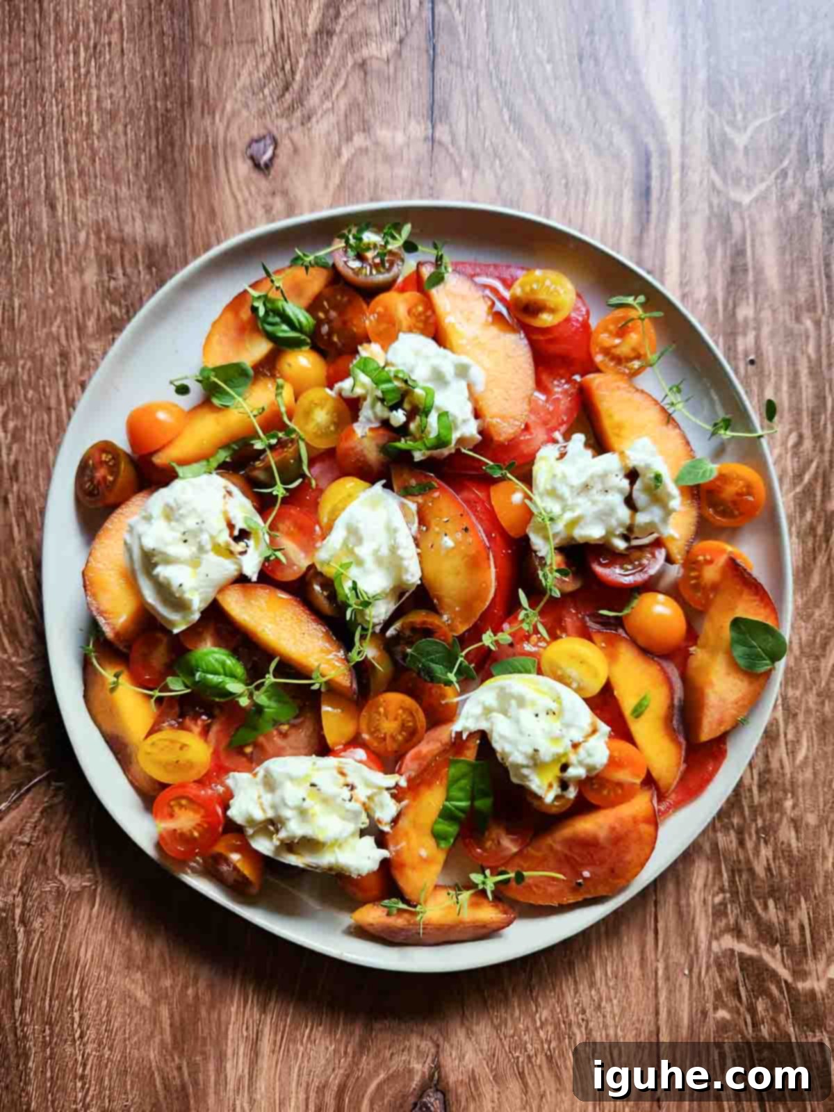 Peaches and Cream Burrata Caprese 7 A completed Burrata Caprese Salad with Peaches on a salad plate, garnished with fresh herbs and a lemon wedge.