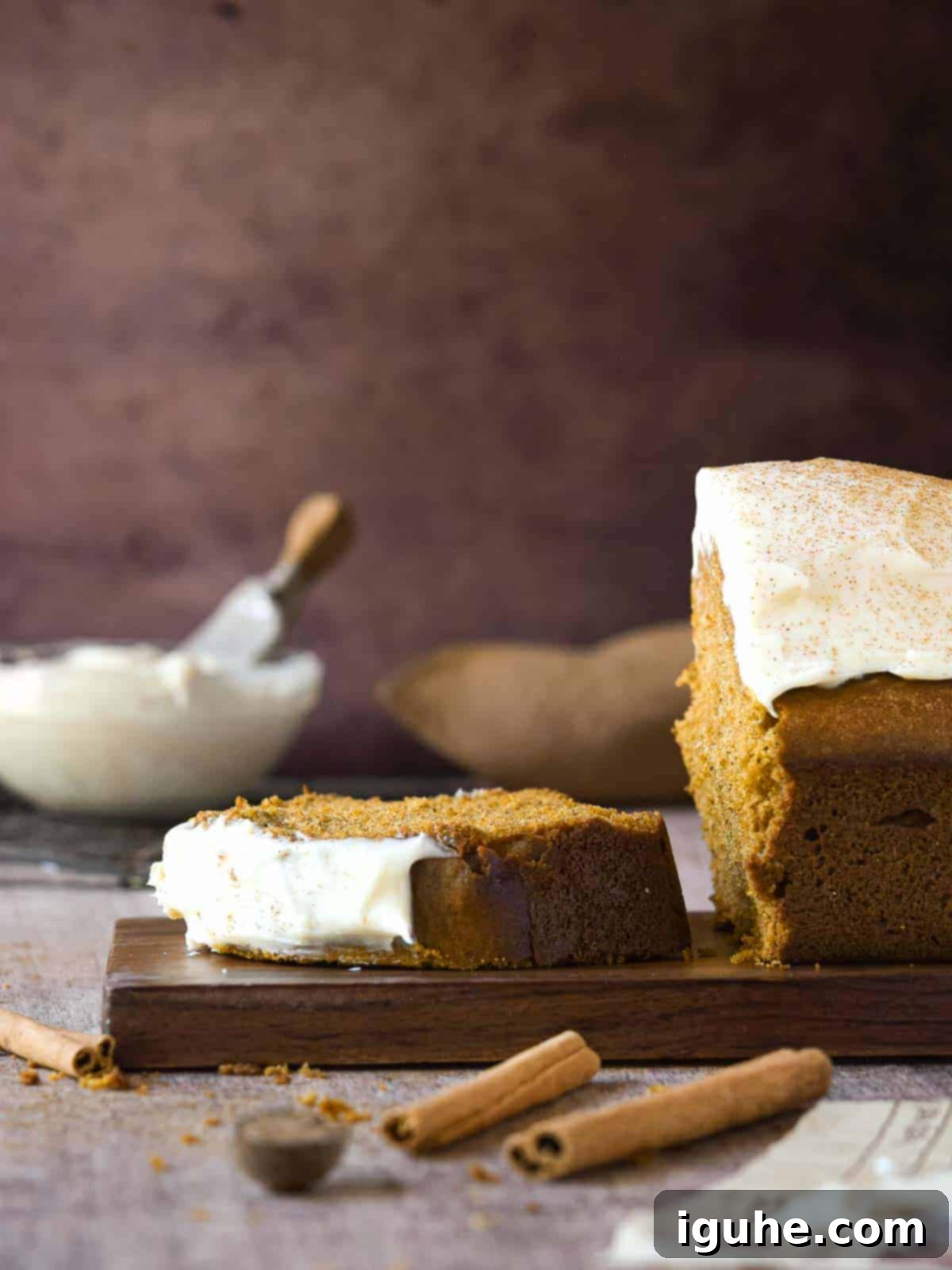 Warm Spiced Pumpkin Bread with Maple Cream Cheese Frosting 3 Side view of pumpkin bread cut, with one slice laying flat with frosting in the background.