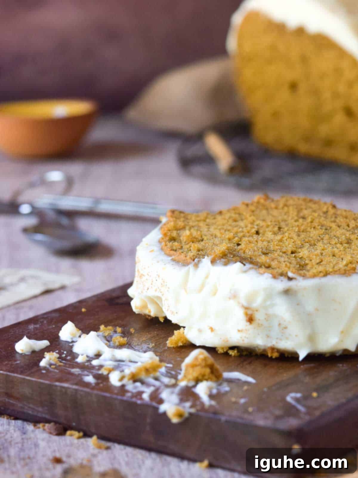 Warm Spiced Pumpkin Bread with Maple Cream Cheese Frosting 9 Close-up of a slice of pumpkin bread with frosting with crumbs on a wood board.