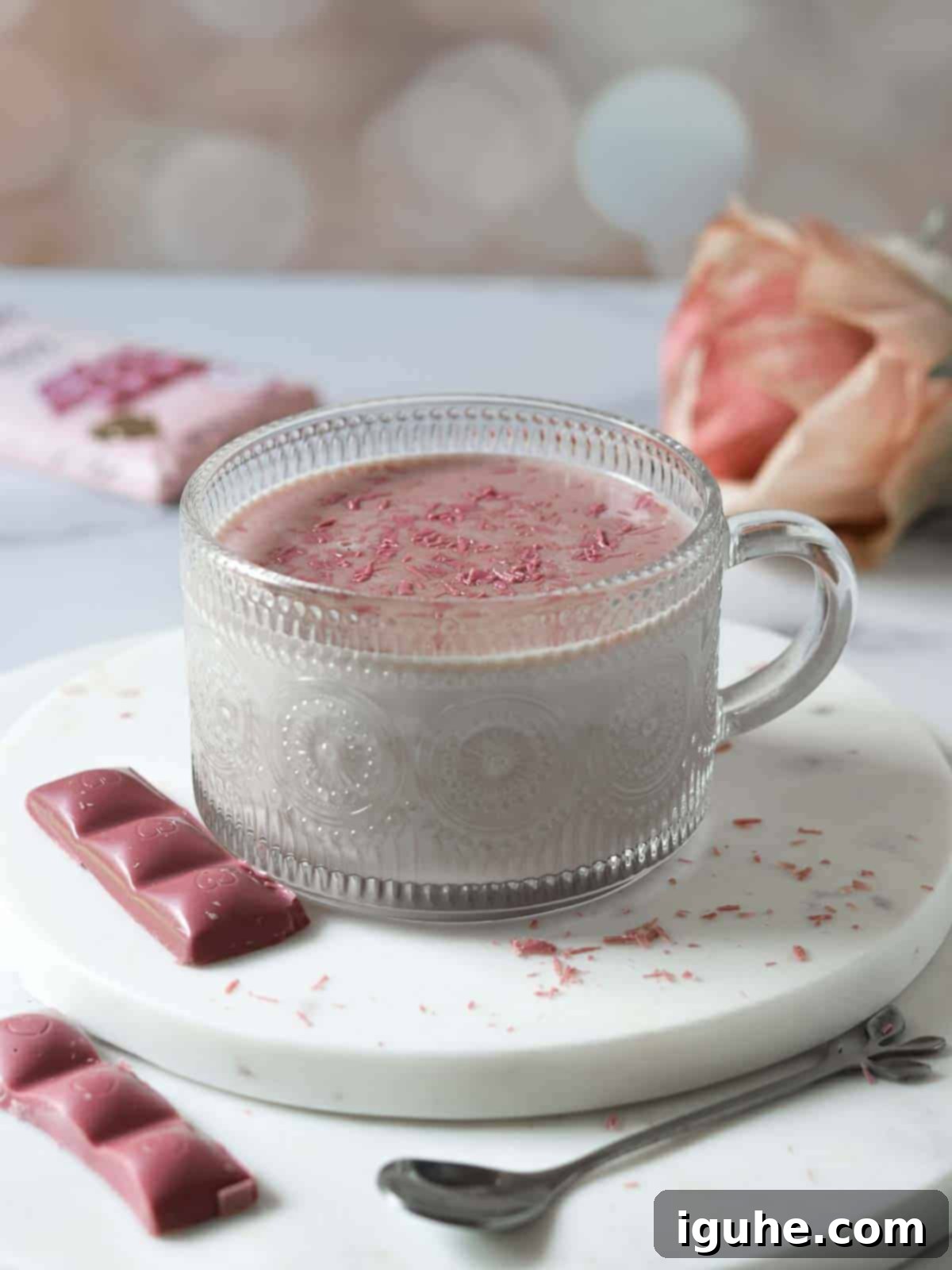 Velvet Ruby Hot Cocoa 7 Ruby hot chocolate in a clear mug on a white surface, garnished with whipped cream.