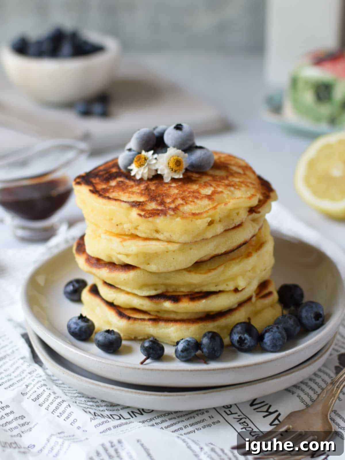 Lemon mascarpone pancakes stacked on plates with blueberries on top, drizzled with syrup.