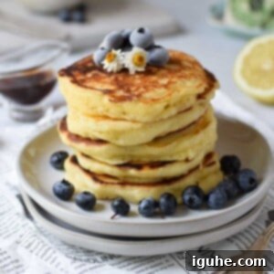 Dreamy Lemon Mascarpone Pancakes 10 Lemon mascarpone pancakes stacked on plates with blueberries on top, ready to be enjoyed.